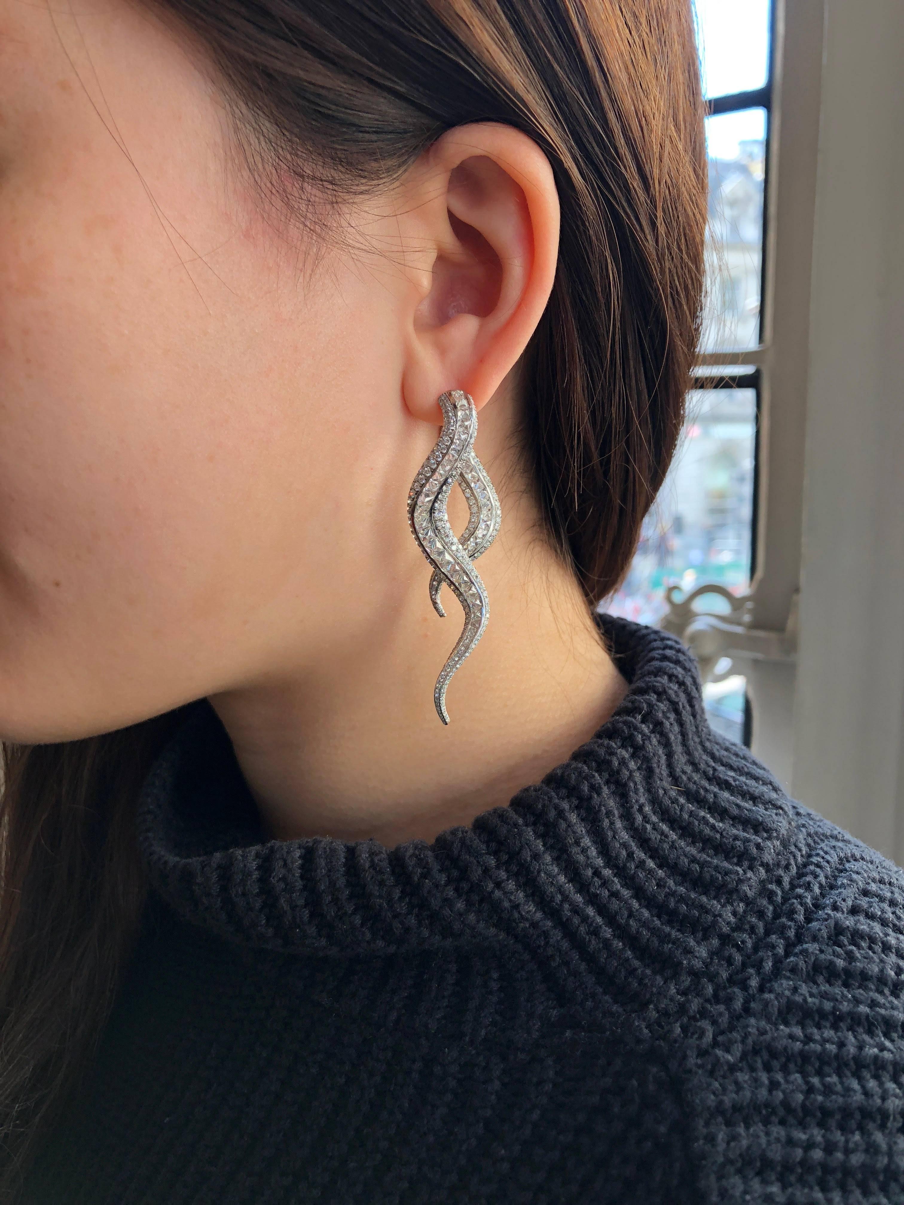 A pair of platinum and diamond snake earrings by Morelle Davidson, each earring designed as a pair of snake tails enveloping the wearer from either side, each tail composed of twisting bands pavé-set alternately with rose-cut or reverse-set