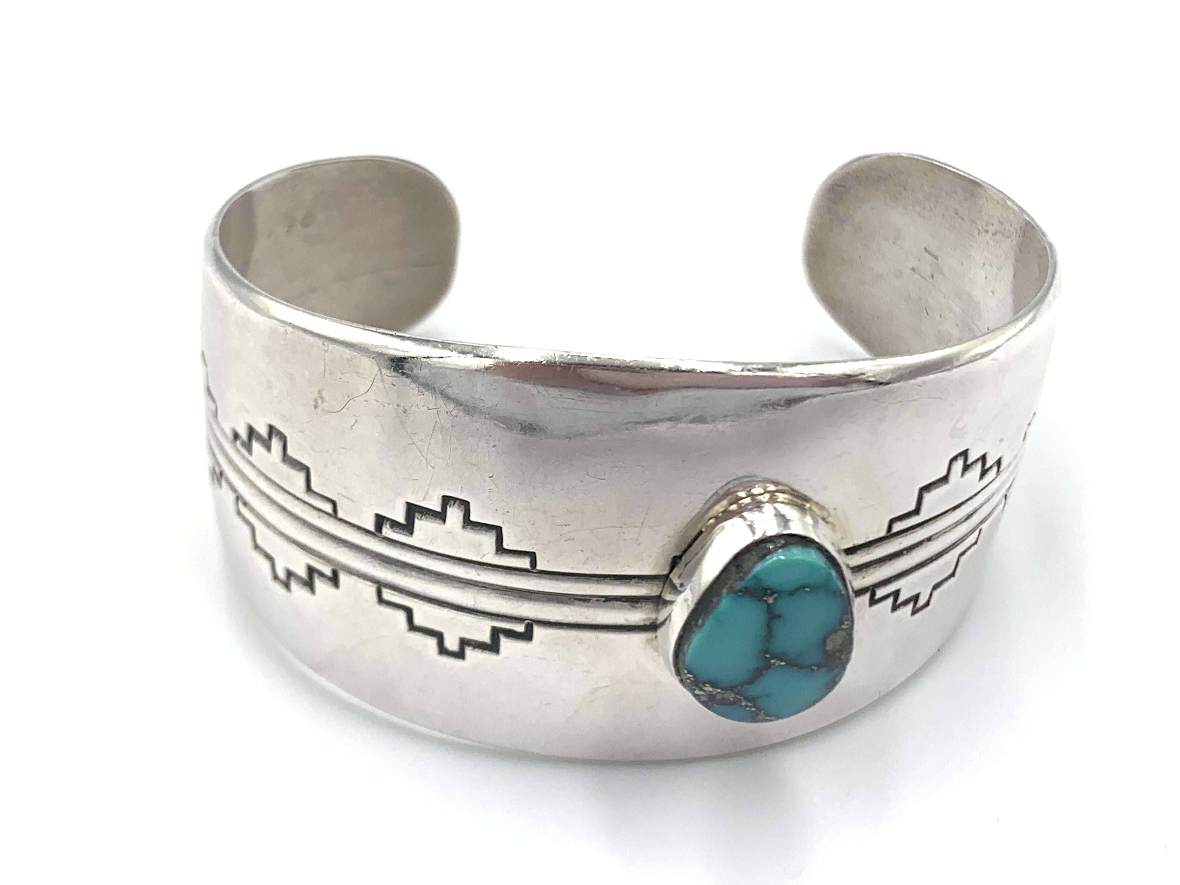Cette magnifique manchette en argent sterling estampillée à la main est ornée d'une vibrante turquoise Morenci, habilement travaillée par l'orfèvre Navajo Jonathon Mike. Le bracelet présente un travail d'estampage géométrique et linéaire raffiné,