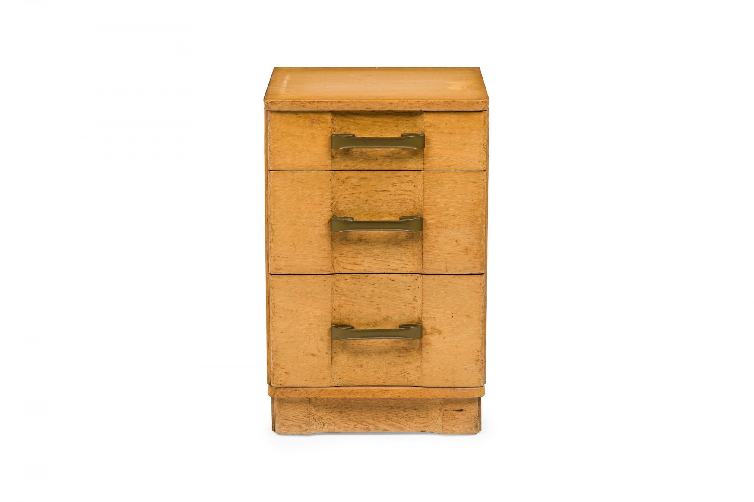 American Mid-Century bedside table / nightstand containing three drawers with recessed center fronts and scroll design brass drawer pulls in a light wooden cabinet with rounded corners and a pedestal base. (MORGAN FURNITURE COMPANY).
 