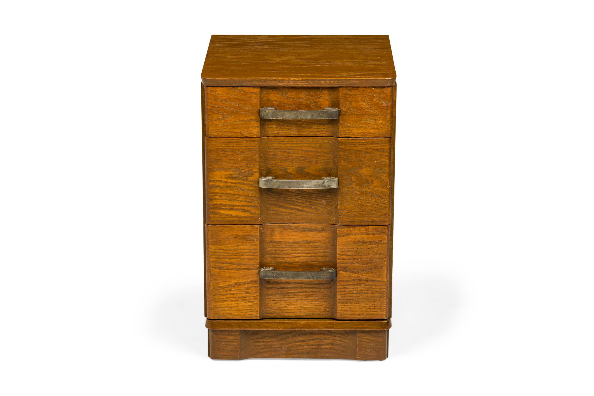 American Mid-Century bedside table / nightstand containing three drawers with recessed center fronts and scroll design brass drawer pulls in a dark stained wooden cabinet with rounded corners and a pedestal base. (MORGAN FURNITURE COMPANY)(Similar