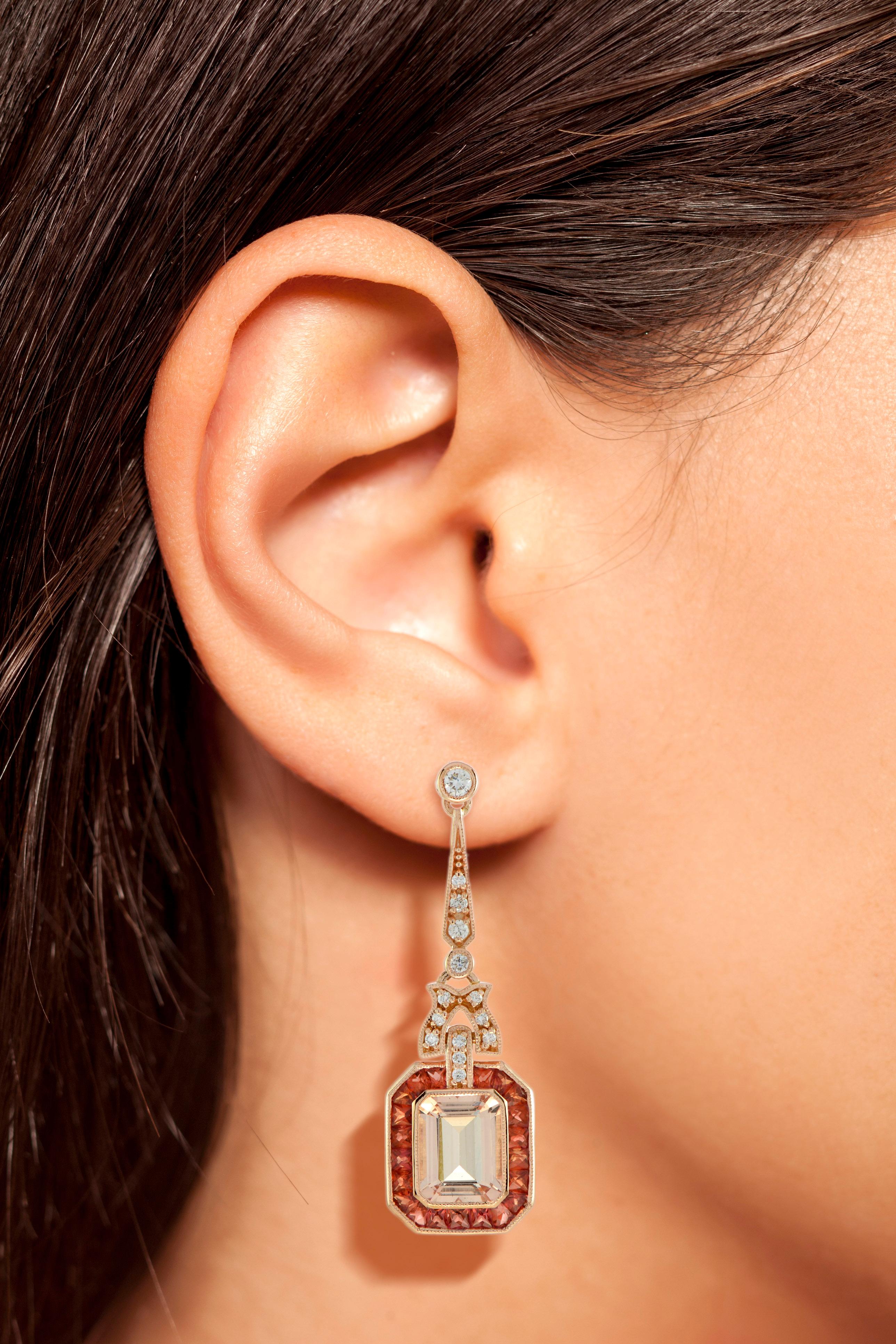 A pair of emerald cut morganite stones, precisely matched by eye, totaling 8.33 carats, and set into a pair of exquisite drop ear studs. These exquisite earrings are complimented by 2.2 carats of French cut orange sapphire and round diamonds