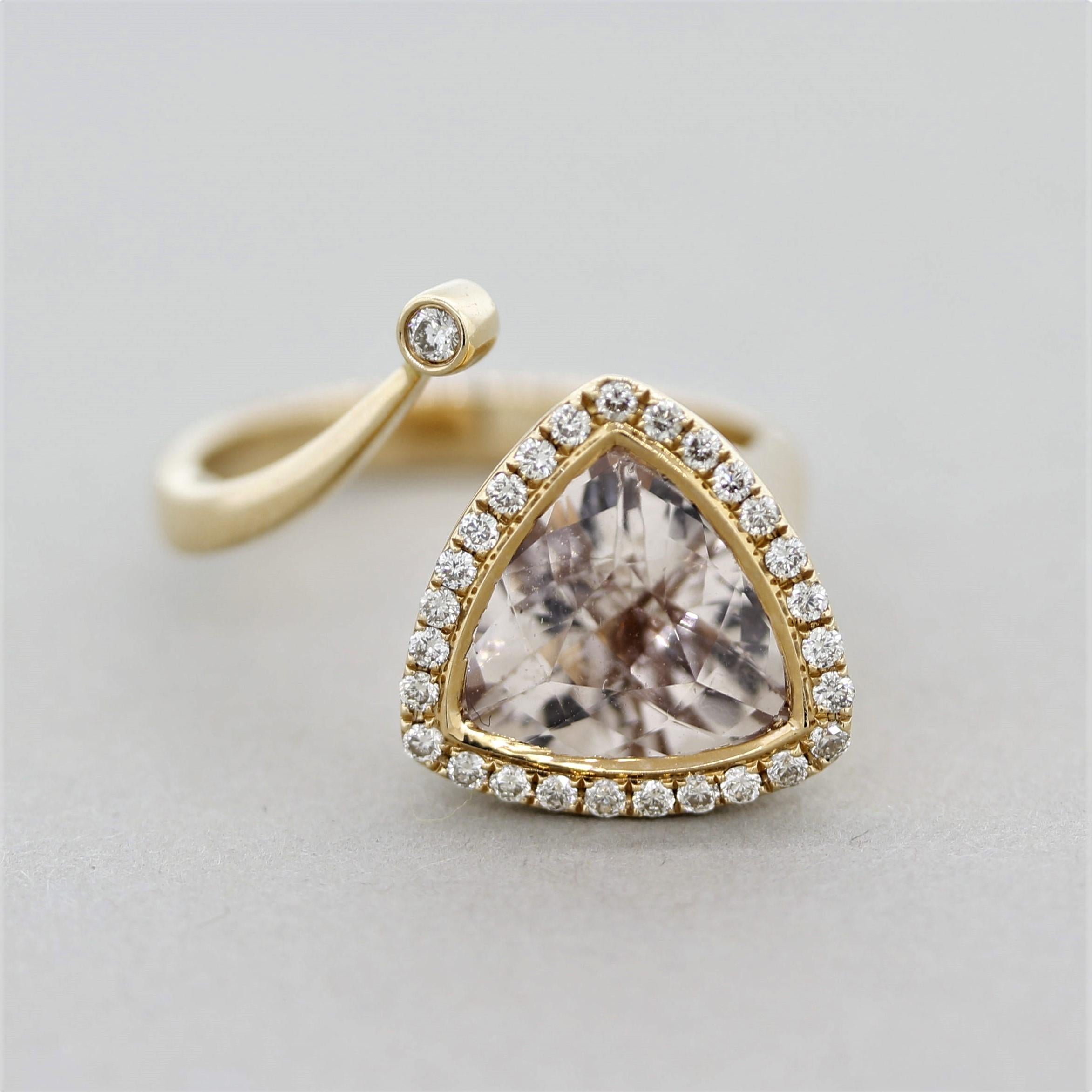 An abstract and unique ring featuring a 3.13 carat trillion-cut morganite. It is bezel set with a diamond halo and accented by a larger diamond set on the opposite end of the ring. Together the round brilliant-cut diamonds weigh 0.27 carats and add