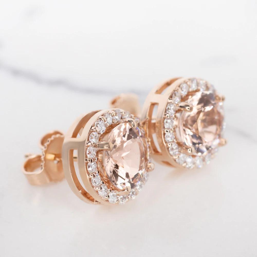 chic pair of studs features natural pink morganites surrounded by halos of vibrant, natural diamonds. The morganites are a beautiful blush color reminiscent of rosé, and their well executed round cuts display gorgeous sparkle. The 14k rose gold