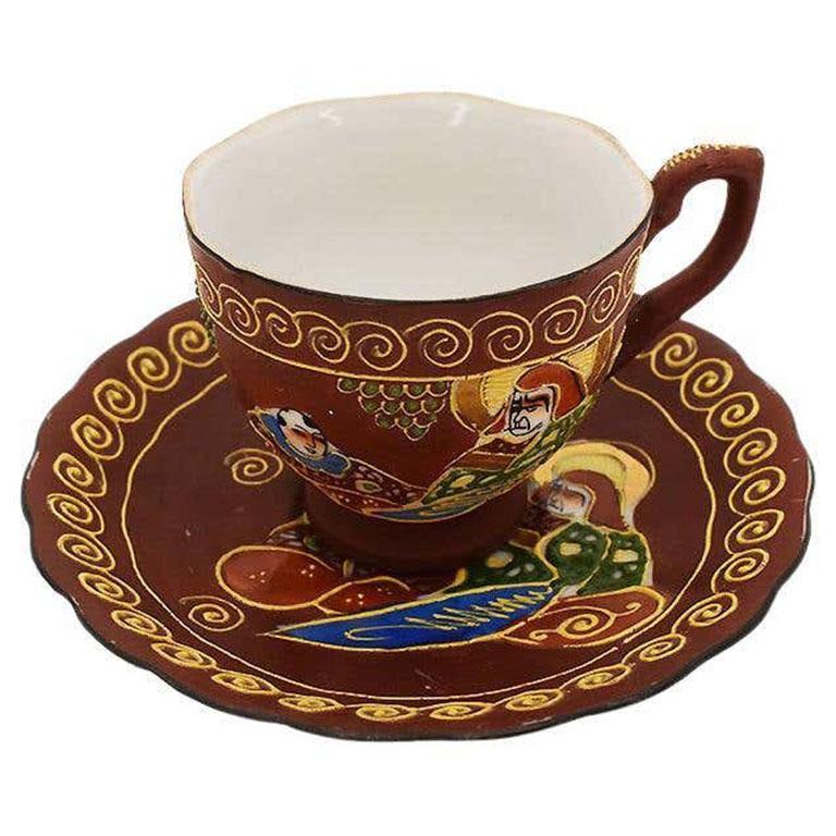 A fine porcelain teacup and saucer set. This pair would be fabulous if mixed in with a current collection, or on its own. On a maroon background, figural and stylized patterns are decorated throughout. The cup features two figures, one in bright