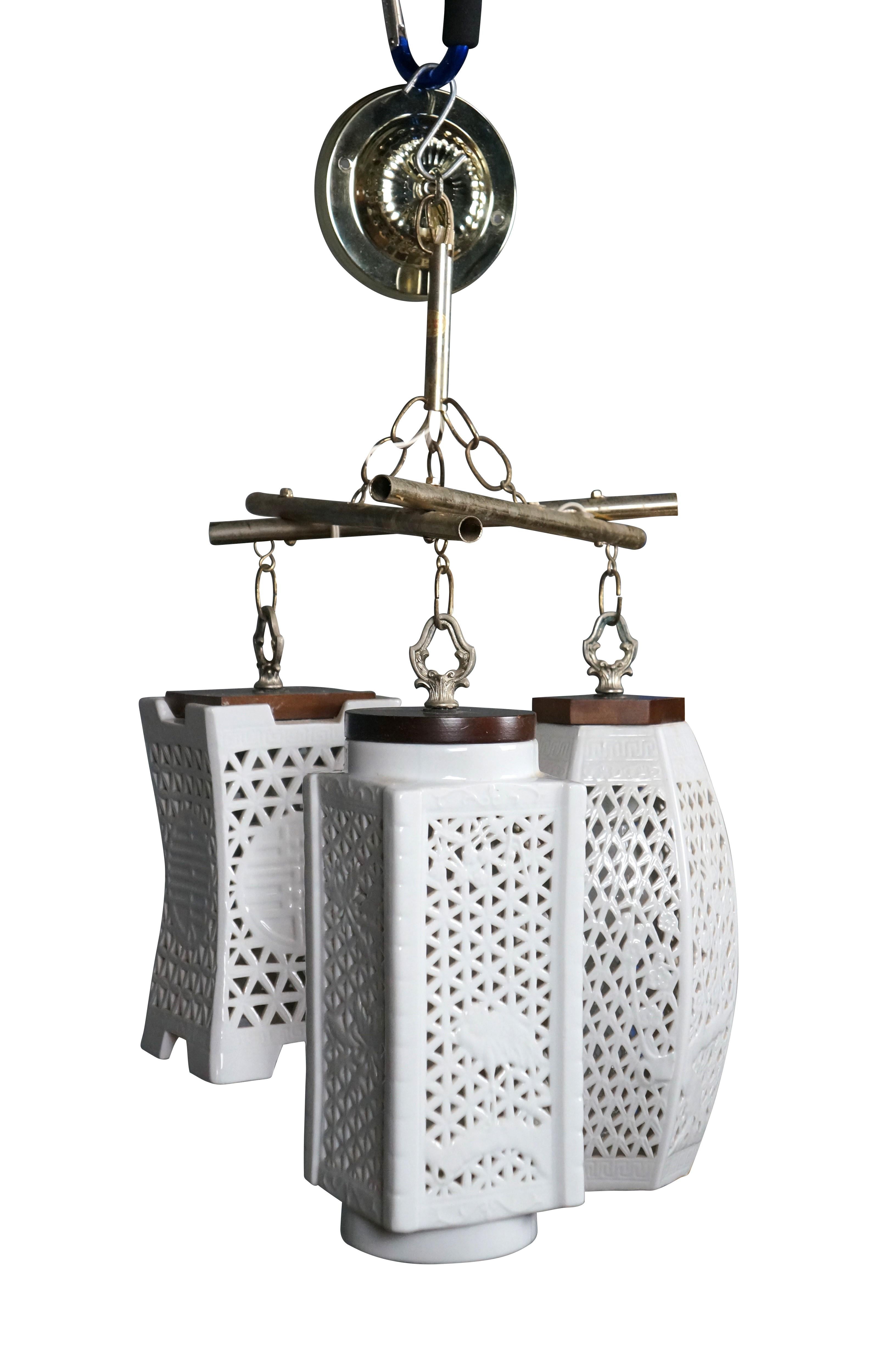 Lampada a sospensione / swag di Morihiro Sangyo, risalente agli anni '50, con un trio di lanterne in porcellana blanc de chine forate di forme diverse, con tappi in legno, sospese da una struttura triangolare in ottone. Una sola luce per ogni