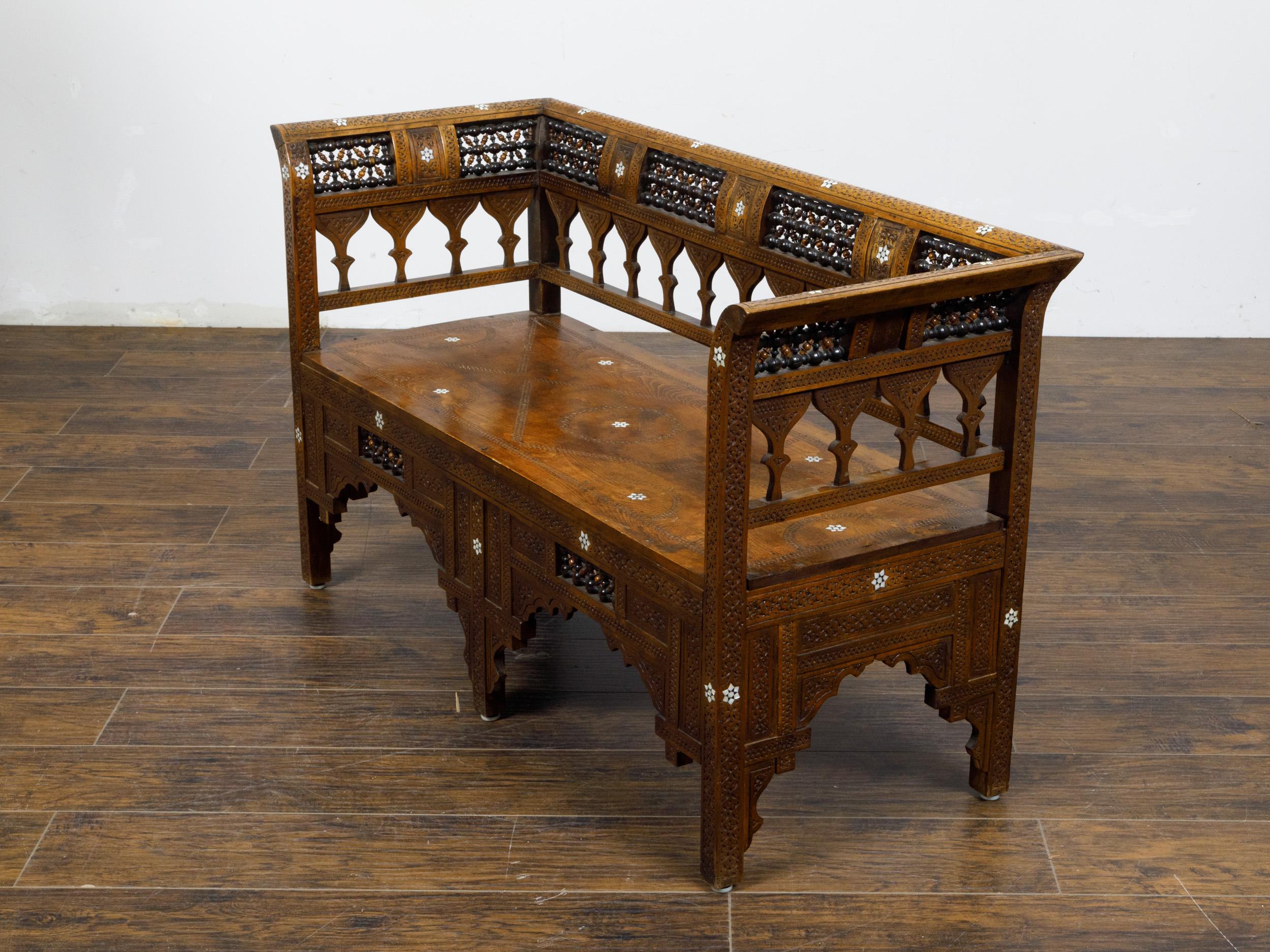 A Moroccan wooden bench with arched backrest, latticework and mother-of-pearl star inlay. This Moroccan wooden bench, dating back to circa 1900, exudes a sense of traditional elegance and intricate craftsmanship. It features a beautifully arched