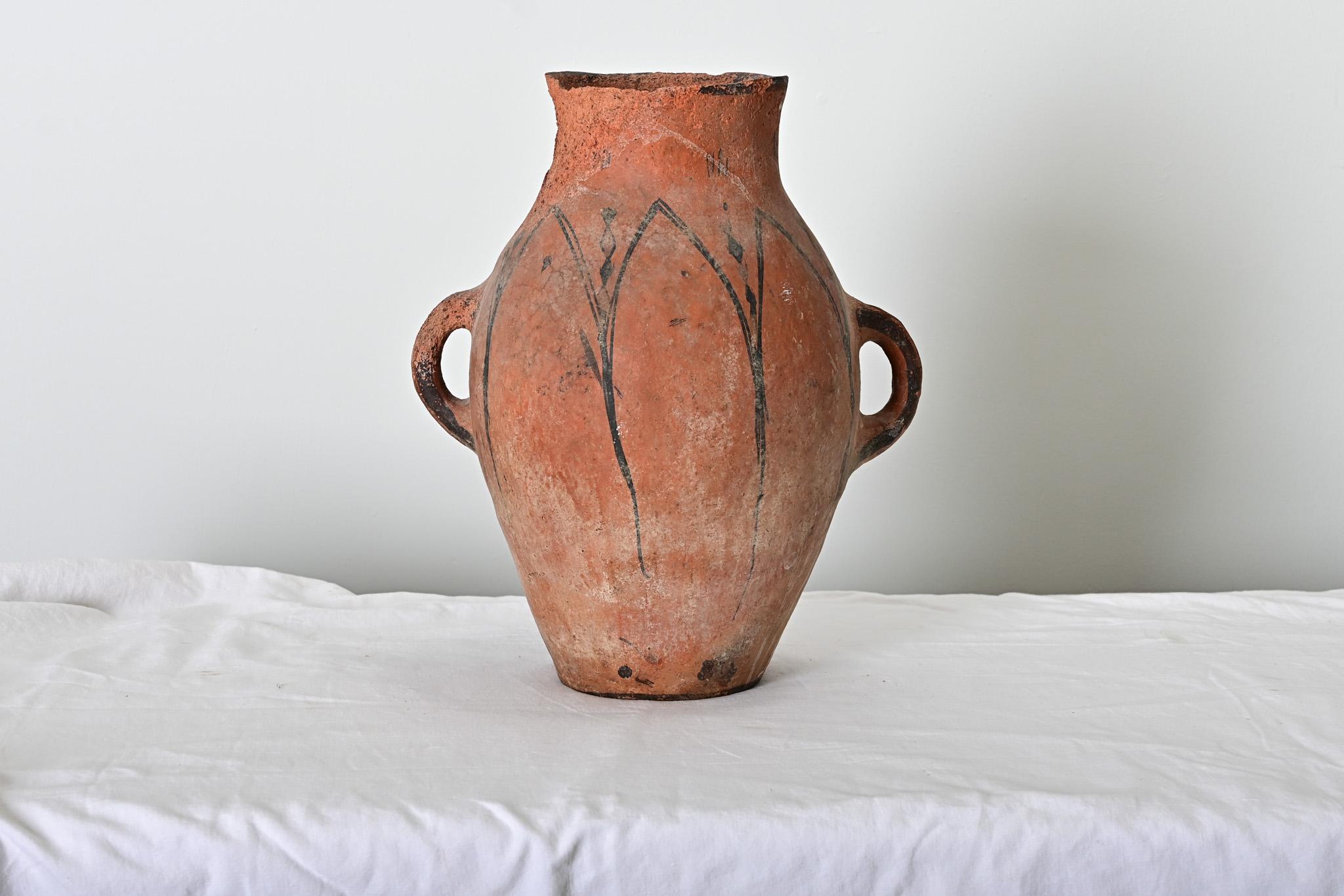 Un recipiente di terracotta fatto a mano proveniente dal Marocco del XIX secolo, con motivi decorativi tradizionali berberi disegnati in nero sull'argilla naturale. Il corpo del pezzo è minimamente decorato con una serie di archi appuntiti,