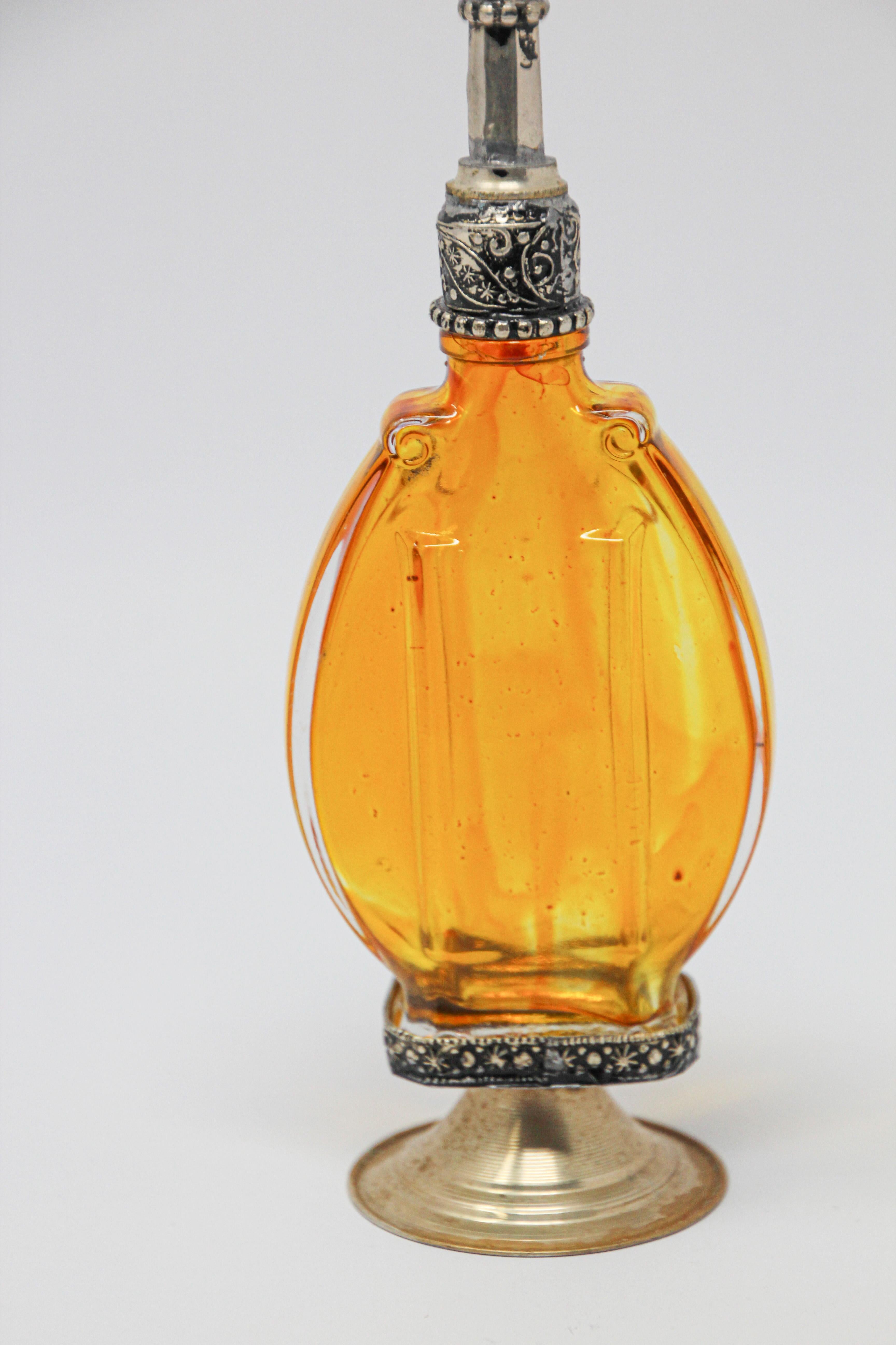 Handcrafted Moroccan Moorish amber painted glass perfume bottle or rose water sprinkler with raised embossed silvered metal floral design over amber glass.
The pressed glass bottle in Art Deco, Art Nouveau style is oval shape with curved sides and