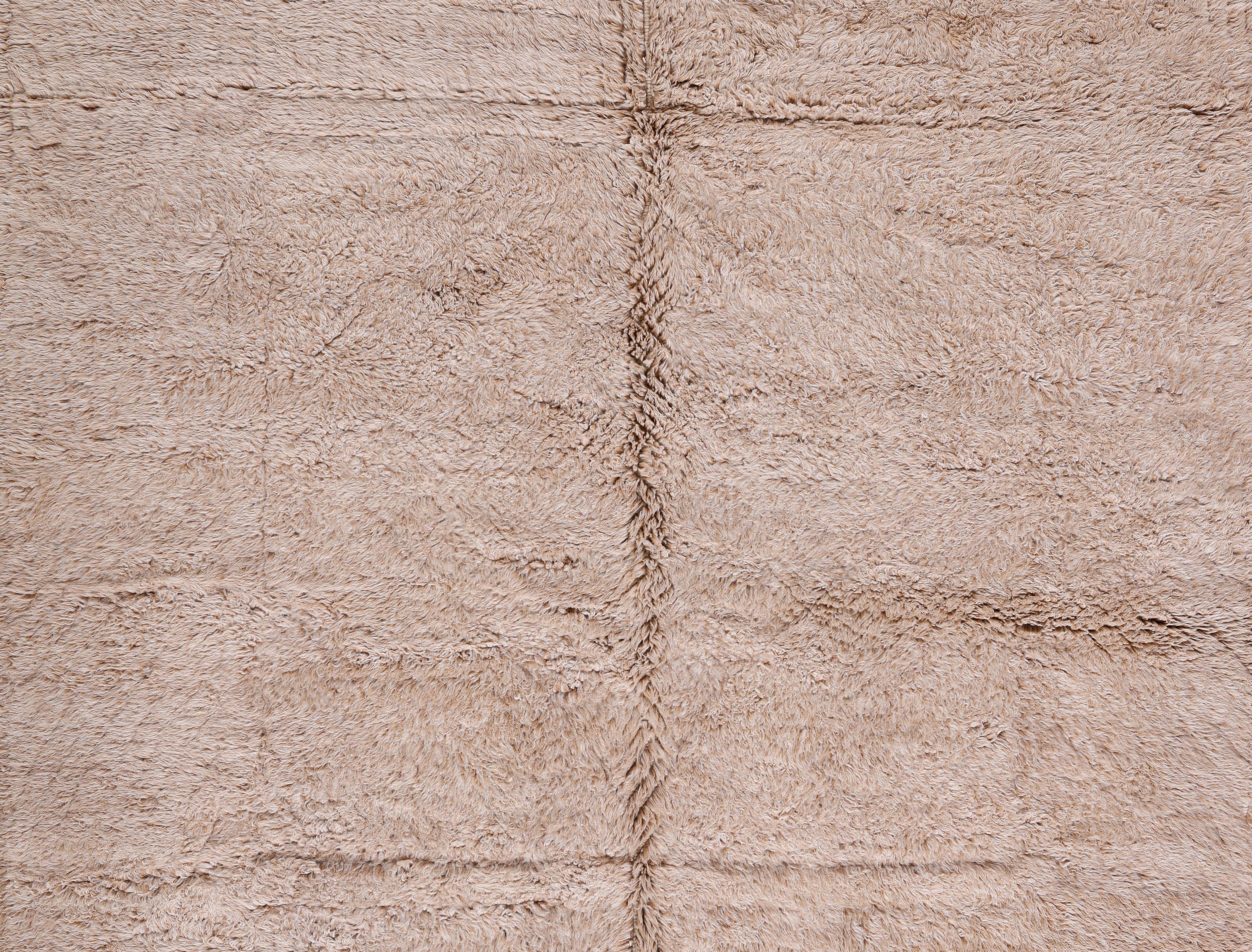 Questo lussuoso tappeto Beni Mrirt, annodato a mano e proveniente dal Marocco, è realizzato al 100% in lana filata a mano, con un vello alto e morbidissimo e una serena tonalità beige naturale. Una sottile struttura di cuciture a griglia aggiunge