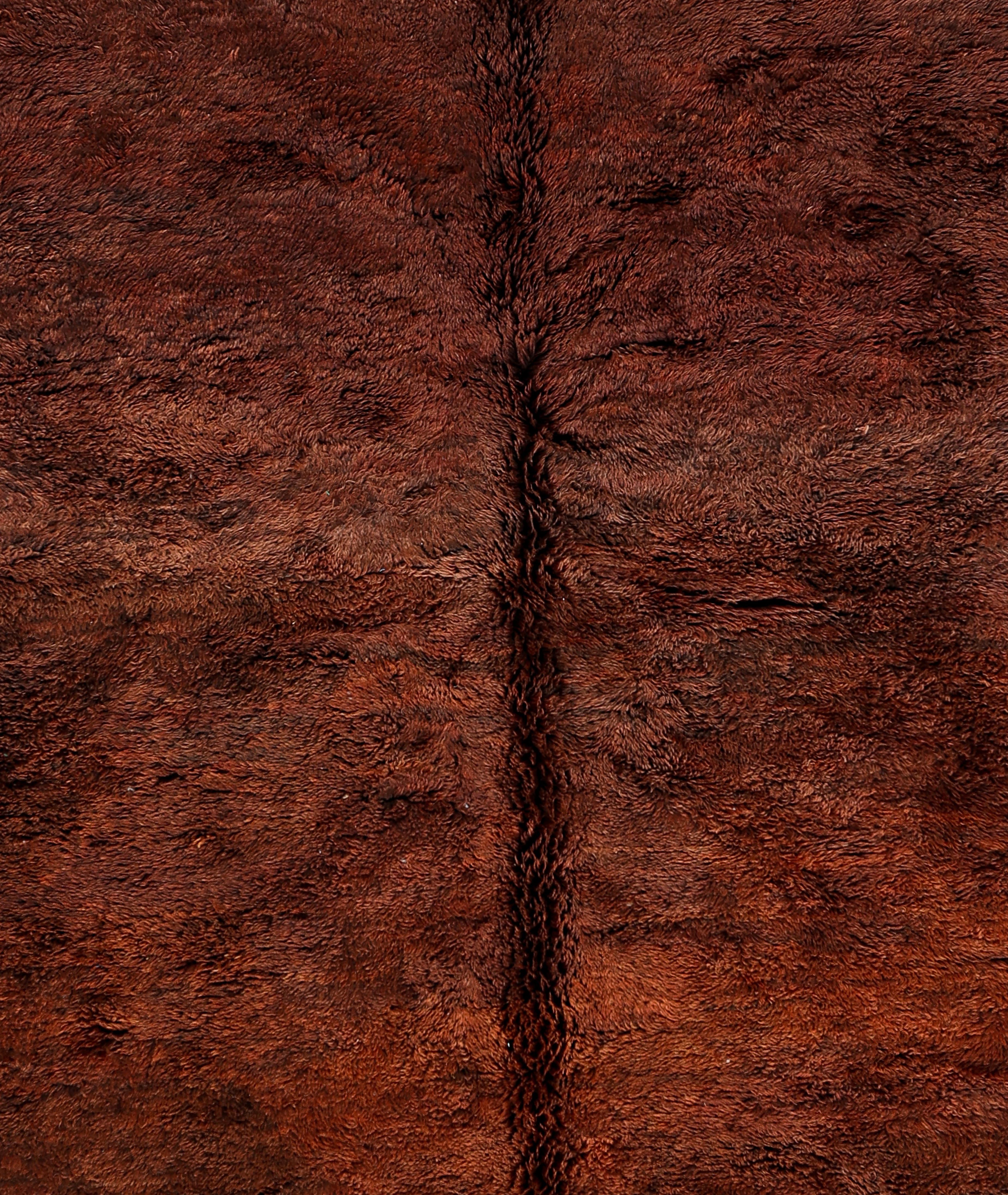 Esta alfombra marroquí Beni Mrirt anudada a mano combina la profundidad minimalista con la sofisticación tribal, presentando un campo de terracota ricamente texturizado enmarcado por atrevidos bordes geométricos en negro y marfil. Fabricada en las