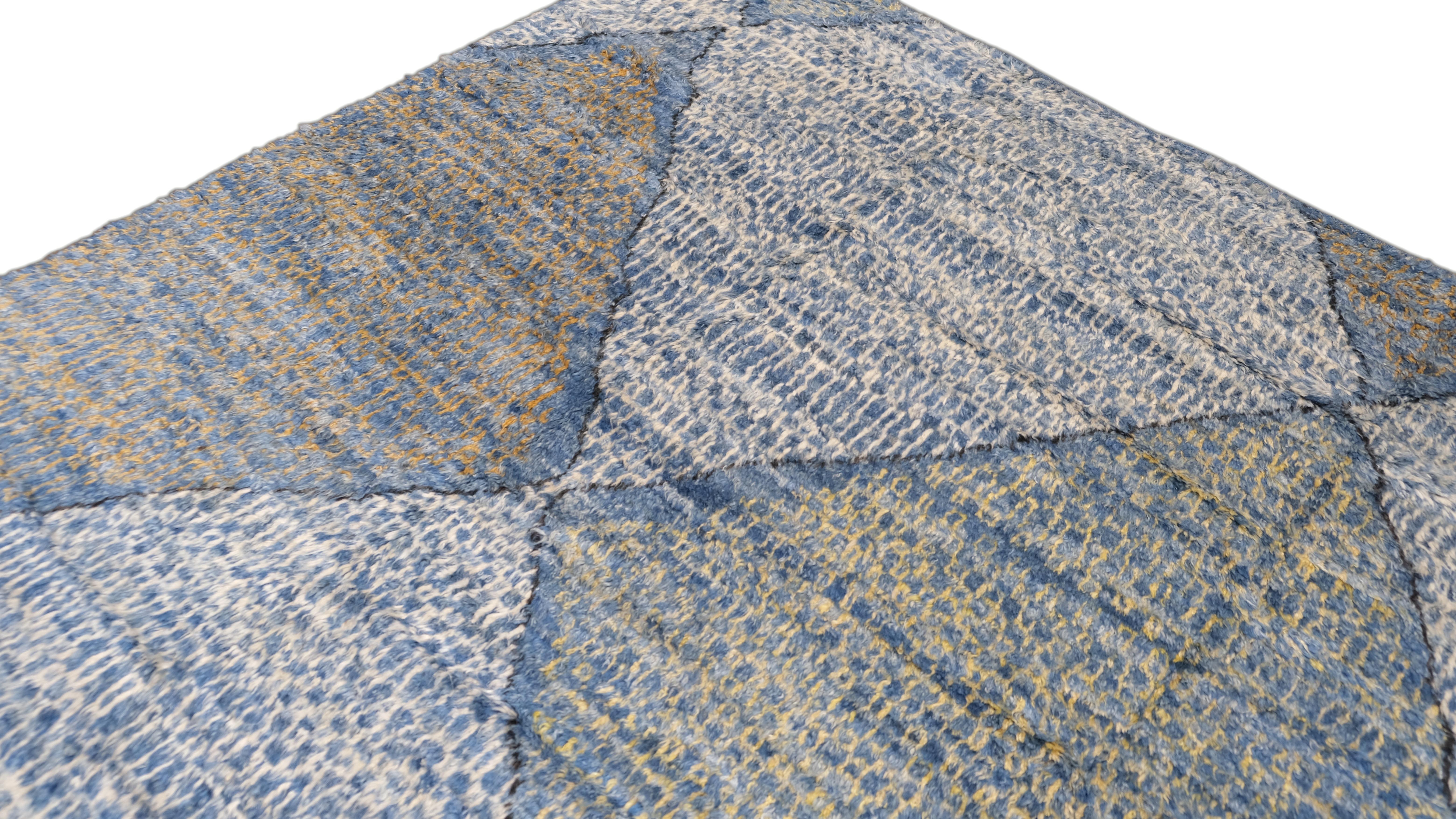 Esta alfombra de lana anudada a mano presenta un llamativo diseño de rombos de inspiración marroquí, tejido en tonos azules y marfil. El diseño geométrico, combinado con la superficie texturizada de la alfombra, crea una estética contemporánea pero