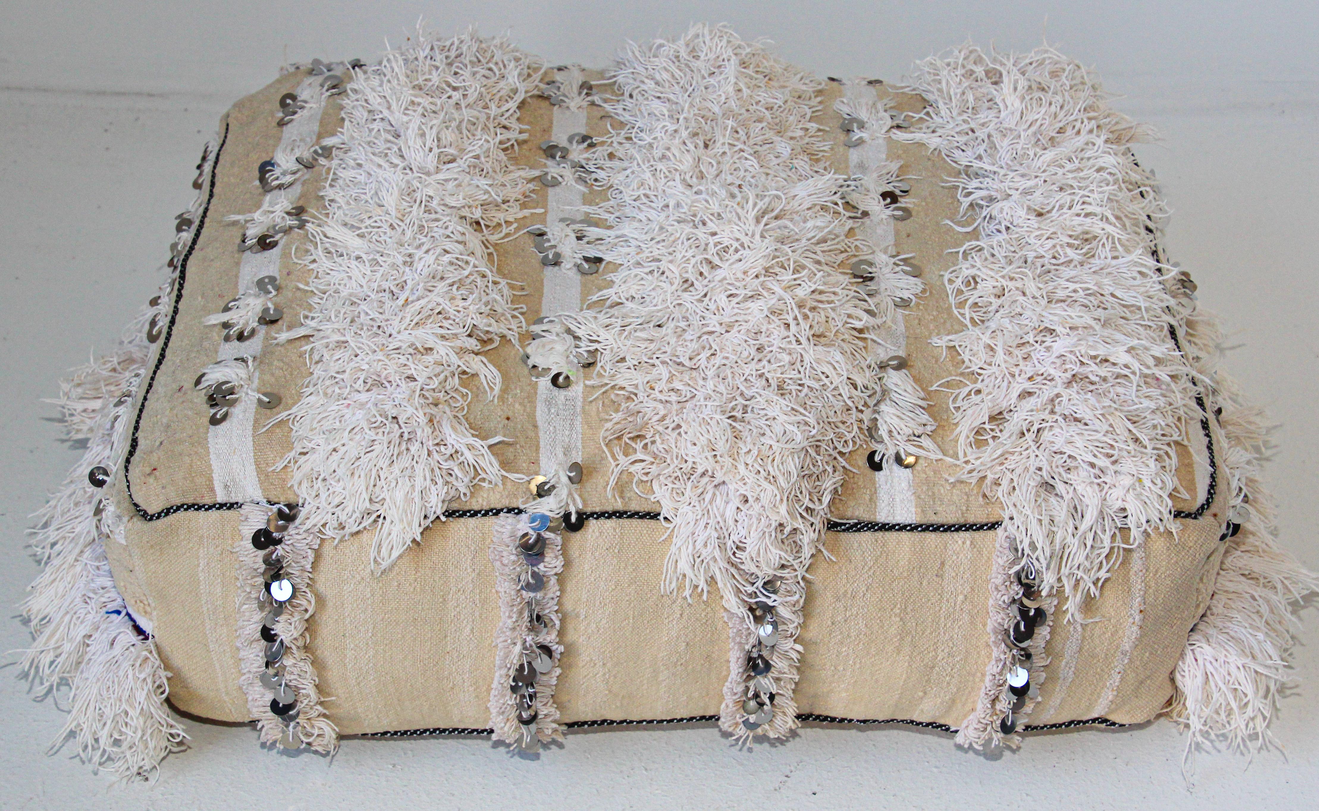 Moroccan wedding floor pillow pouf with silver sequins and long fringes.
Bohemian handcrafted vintage Moroccan tribal floor pillow or pouf made from a traditional handwoven white wool and cotton throw used by the Berber women in Morocco for their