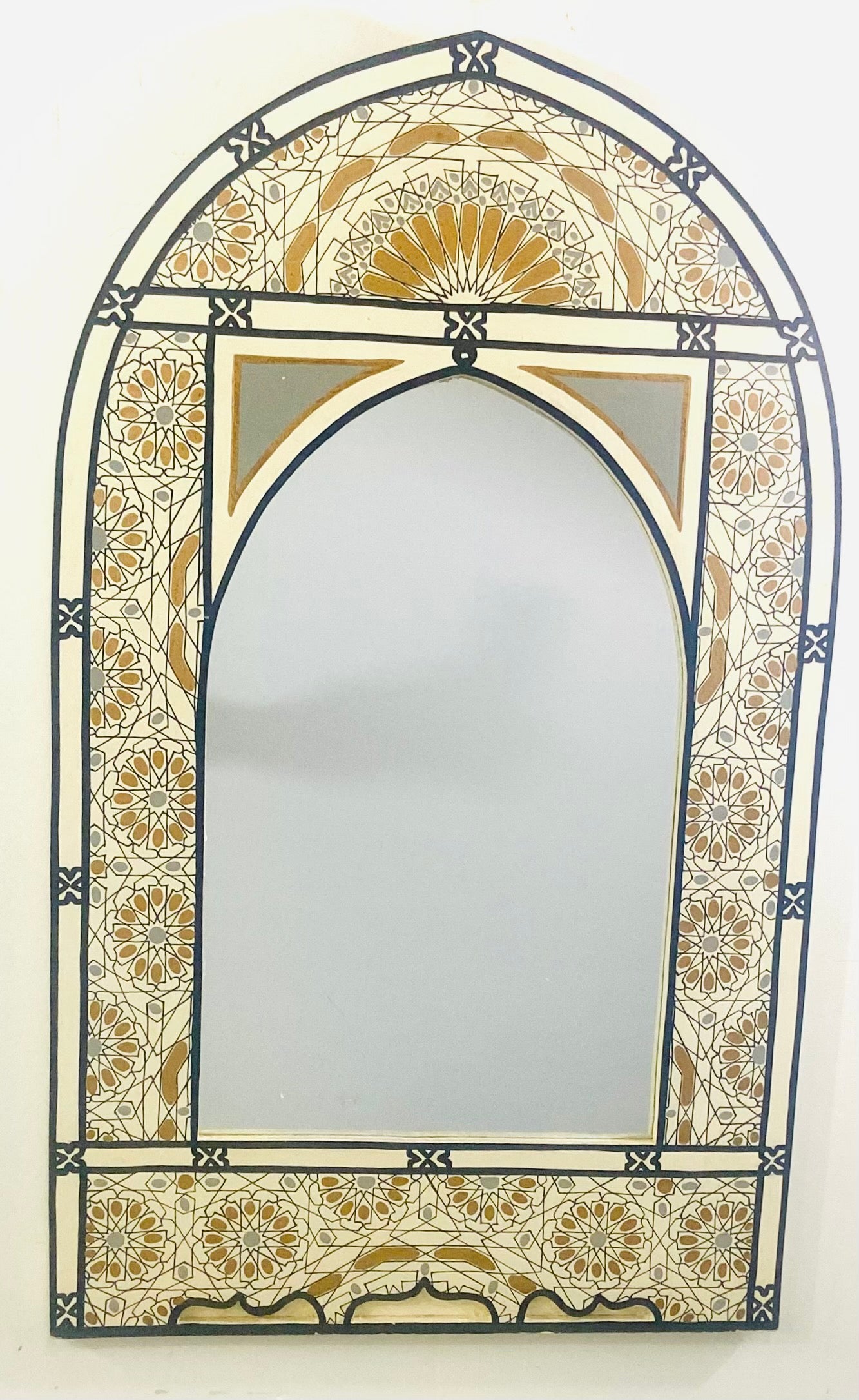 A beautiful Bohemian style Moroccan wall, table or vanity mirror. The mirror frame is hand carved in a timeless Moorish arch shape and artistically hand-painted to feature intricate Moorish geometrical designs in blue gray, black and gold. The