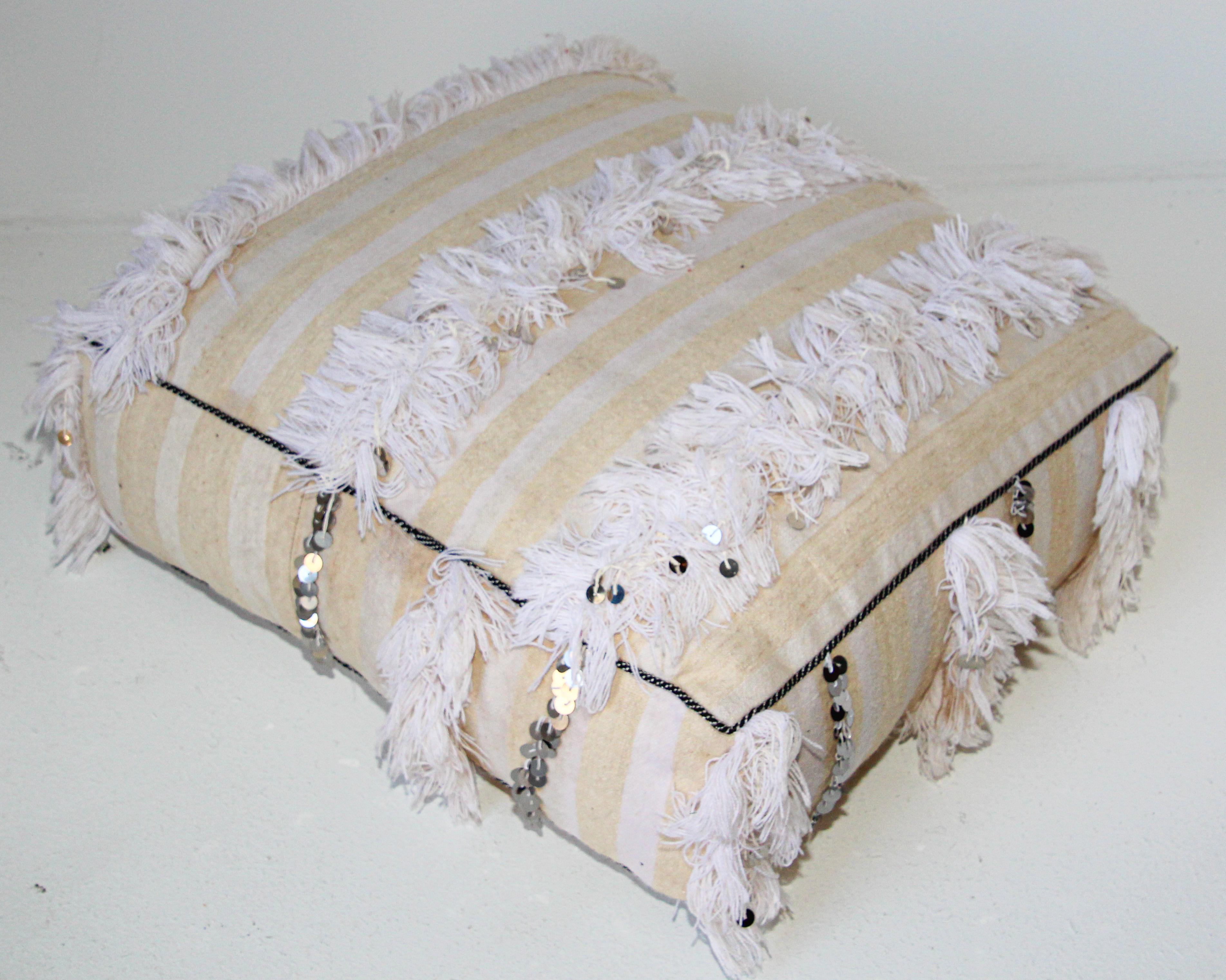 Moroccan wedding floor pillow pouf with silver sequins and long fringes.
Bohemian handcrafted vintage Moroccan tribal floor pillow or pouf made from a traditional handwoven white wool and cotton throw used by the Berber women in Morocco for their
