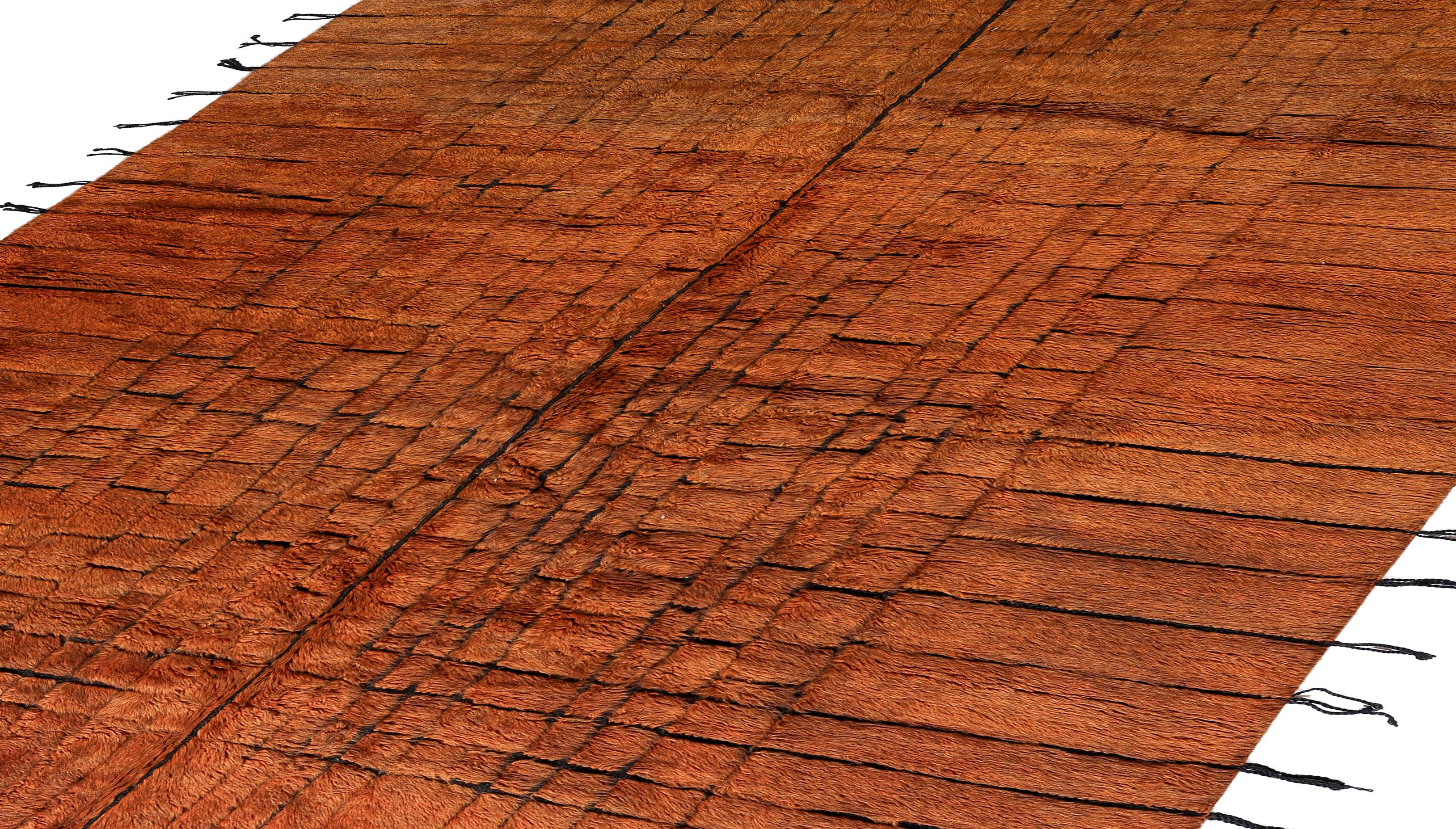 Anudada a mano en las montañas del Atlas, esta auténtica alfombra marroquí muestra un cálido campo naranja quemado enriquecido por una cuadrícula en capas de suaves motivos lineales y a cuadros. Los sutiles detalles negros añaden profundidad y ritmo