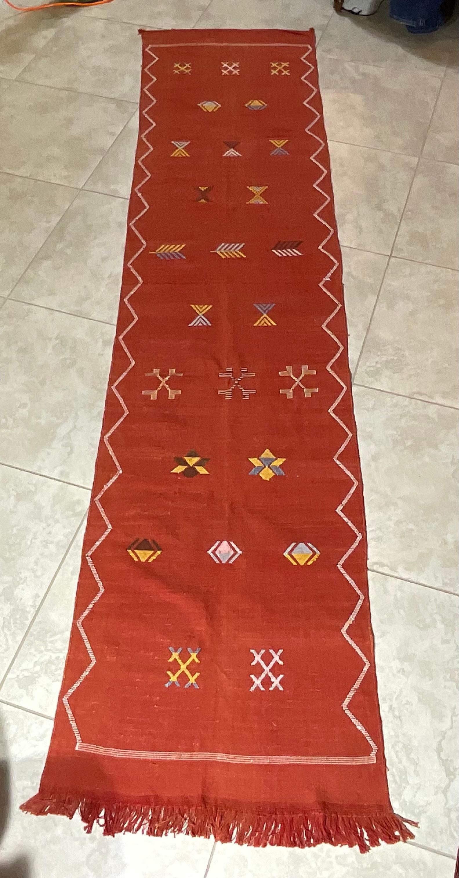 Preciosa alfombra tejida a mano en seda de cactus con suaves motivos geométricos multicolores sobre un fondo de color rojo-salmón, agradable al tacto. Gran complemento decorativo para cualquier habitación.