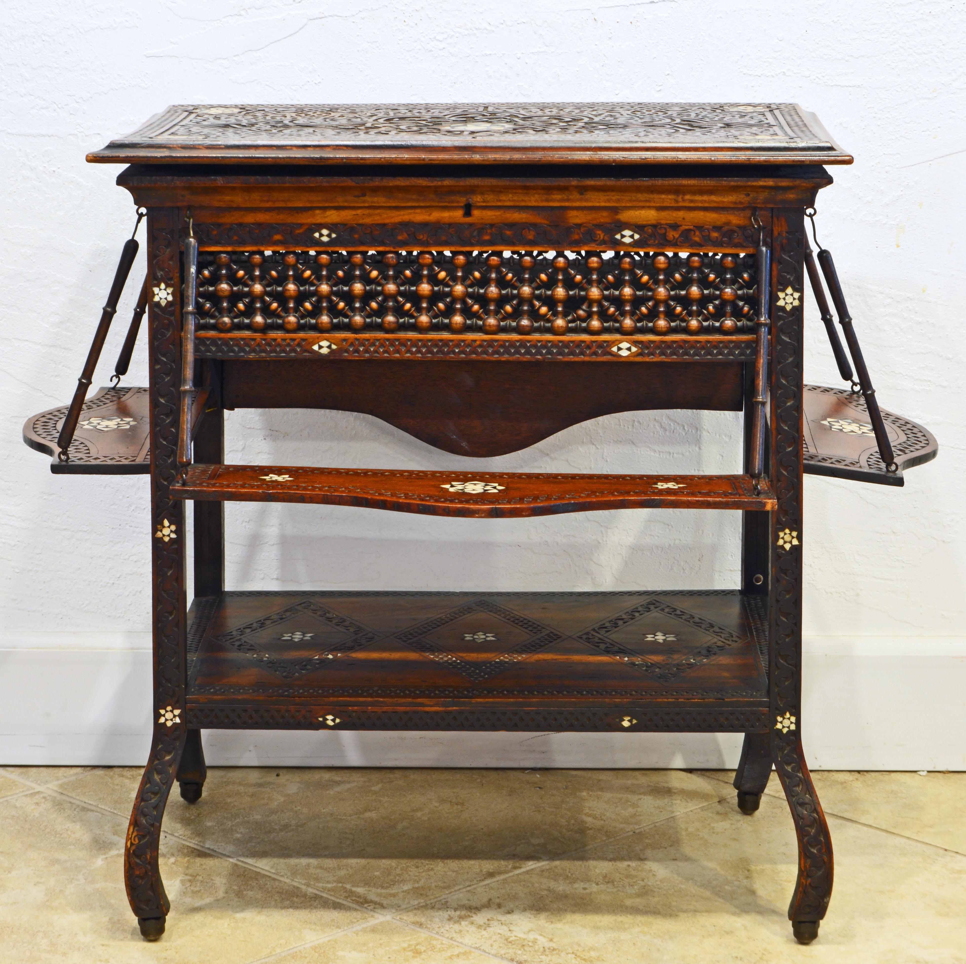 This unusual Moroccan aside table features a richly carved and inlaid top that opens up to a storage compartment above fretwork aprons and a second lower tier. On three sides there are suspended extra shelves, a feature found in several Middle East