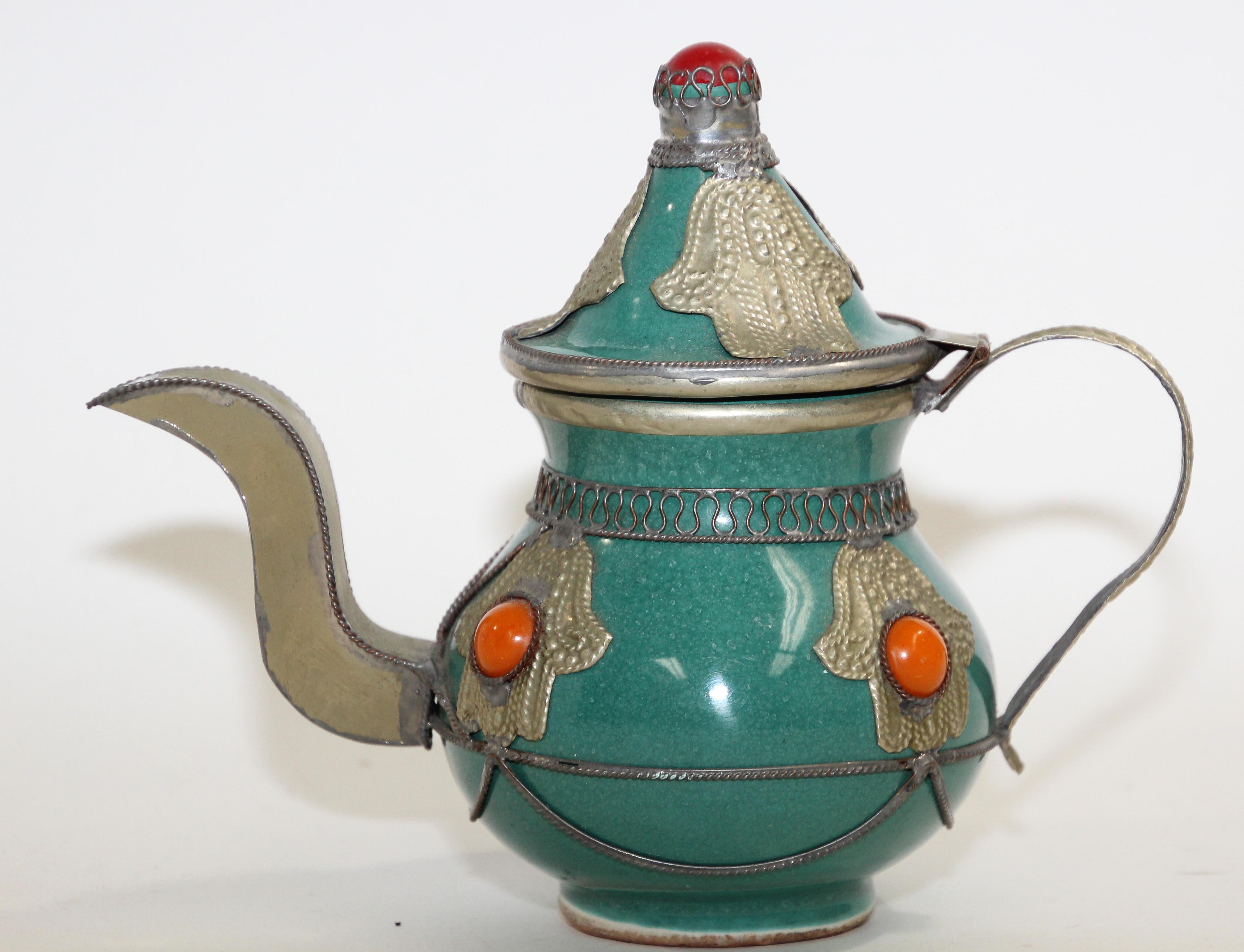 Traditional vintage blue teal color ceramic and silver metal filigree Moroccan tea pot.
Decorative tea pot with traditional overlay silver design with metal Khamsa, the protective Hand of Fatima and orange color stones, handcrafted in Fez.
Great