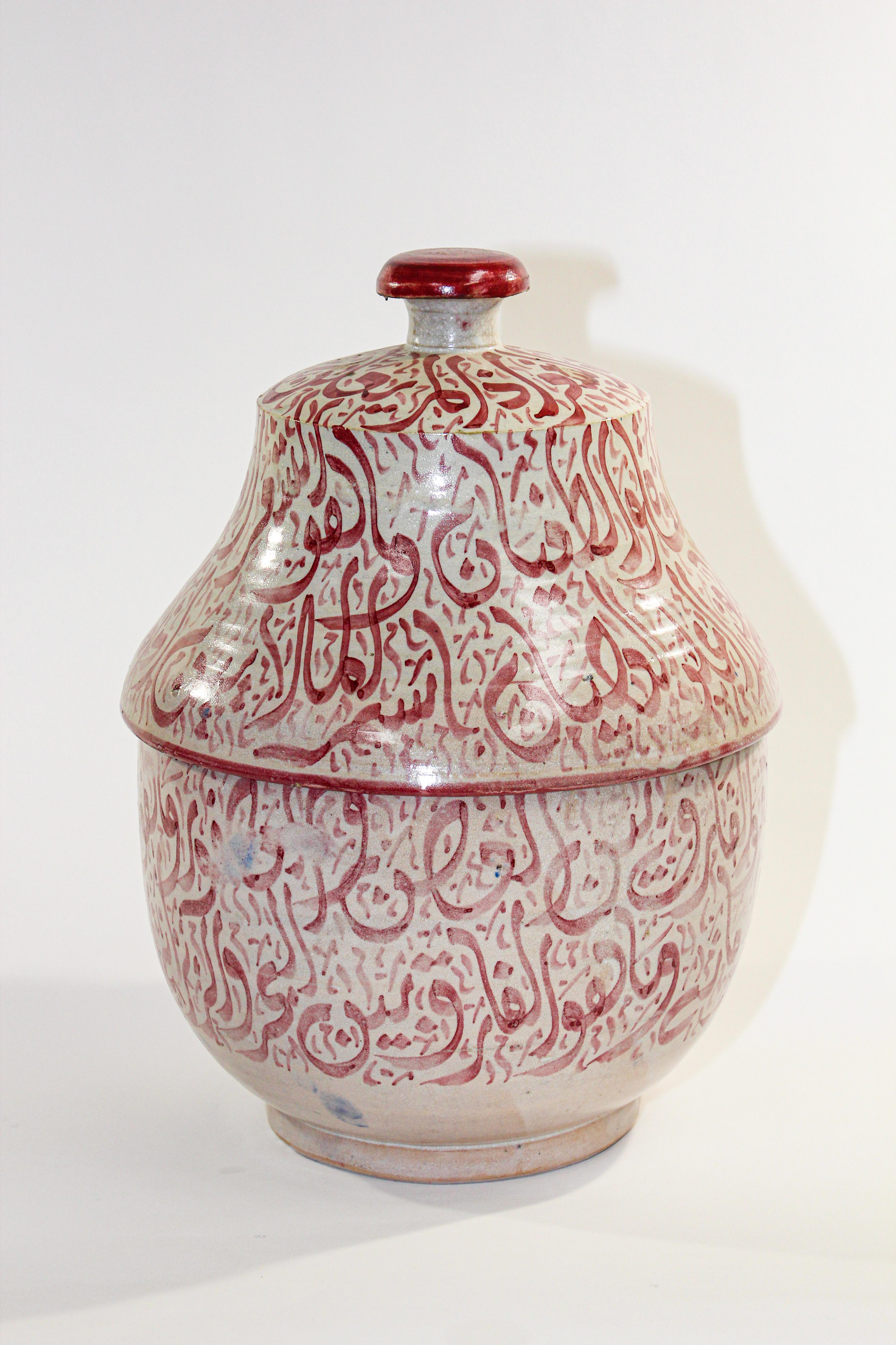 Urne marocaine en céramique émaillée avec couvercle, provenant de Fès. 
Céramique de style mauresque fabriquée et peinte à la main avec une écriture arabe calligraphiée en rose.
Ce type d'écriture calligraphique s'appelle le Lettrisme, c'est une