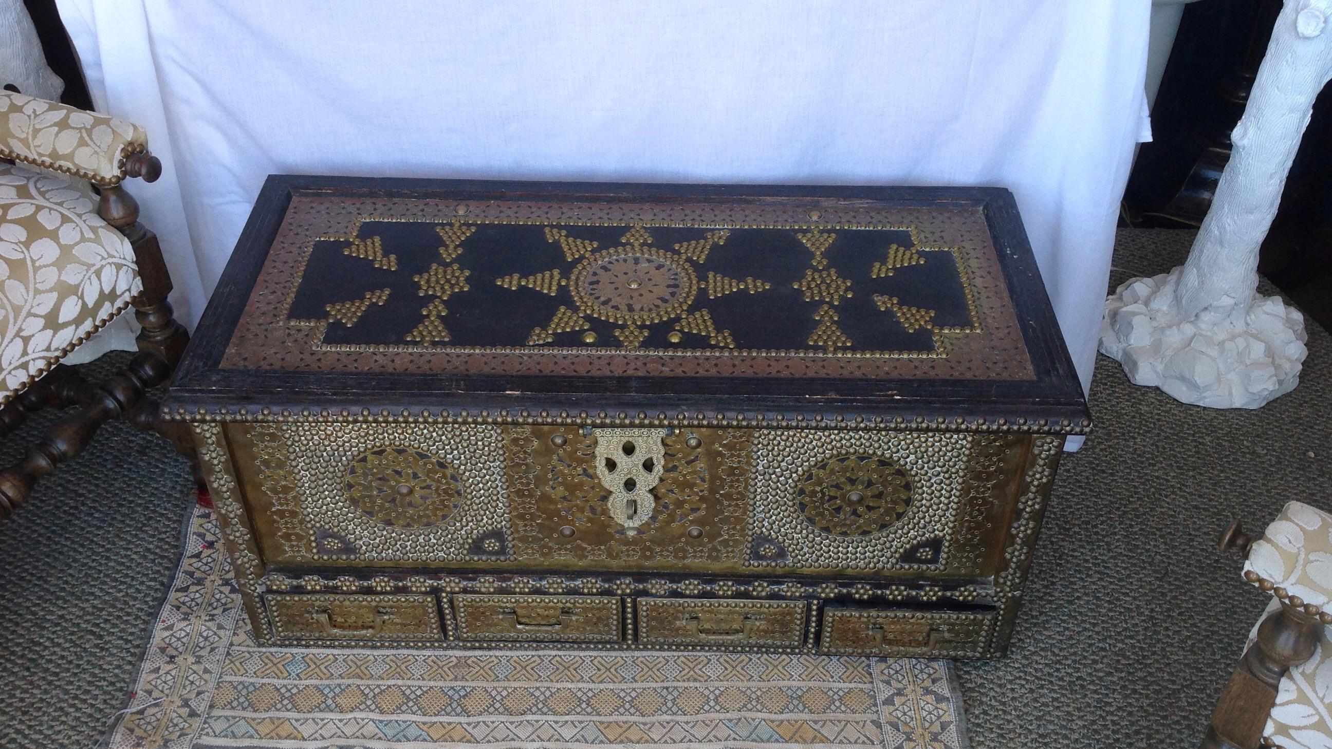 Fashioned with elaborate applied brass work, nail head design as well as brass 
handles - the trunk is also designed with four bottom drawers and has 4 attachable 
feet to raise the trunk off the ground.