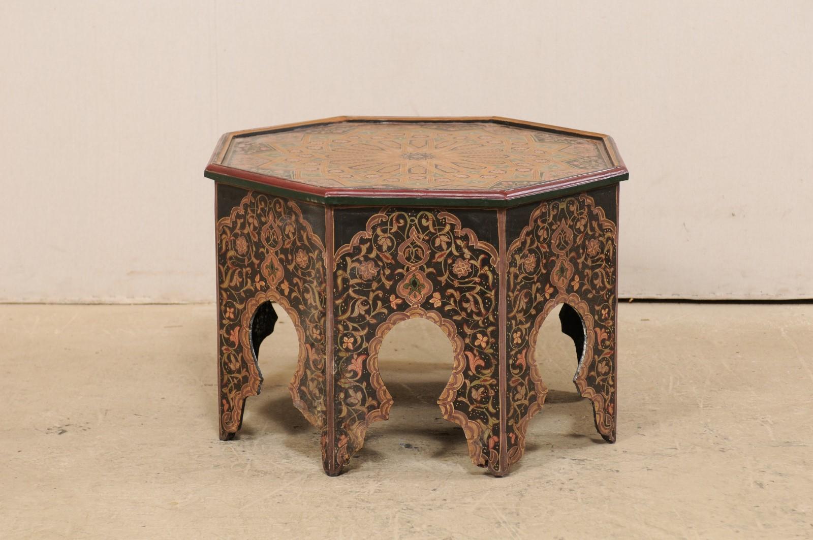 A vintage Moroccan coffee or tea table delicately hand painted in intricate floral and geometric designs. This octagonal-shaped side table from Morocco features a multi-colored floral and geometric designed top, with raised lip about perimeter
