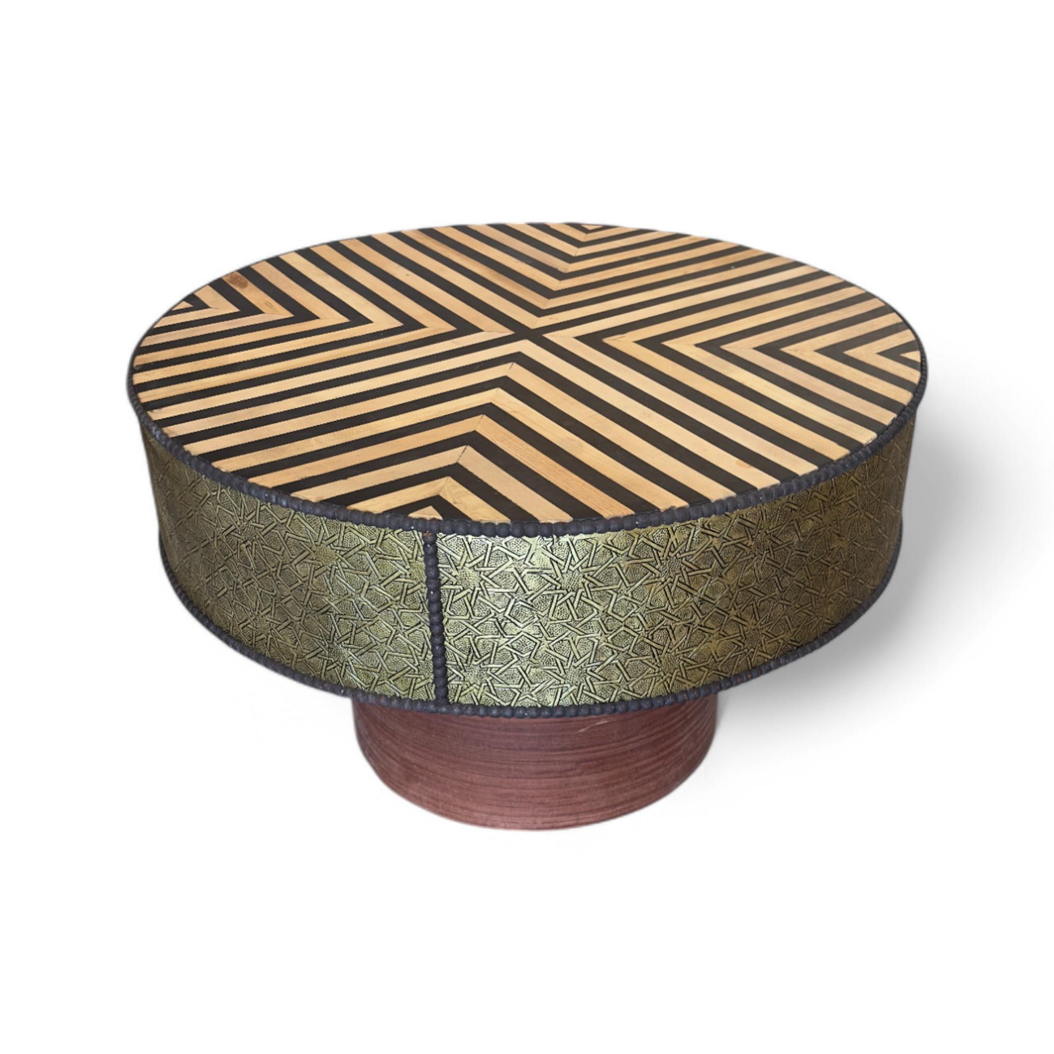 Ein auffälliger runder marokkanischer Couchtisch, der handwerkliche Kunstfertigkeit mit kühnem geometrischem Flair verbindet. Die mit Intarsien versehene Holzplatte steht in schönem Kontrast zu einer handgefertigten, messingfarbenen Umrandung, die