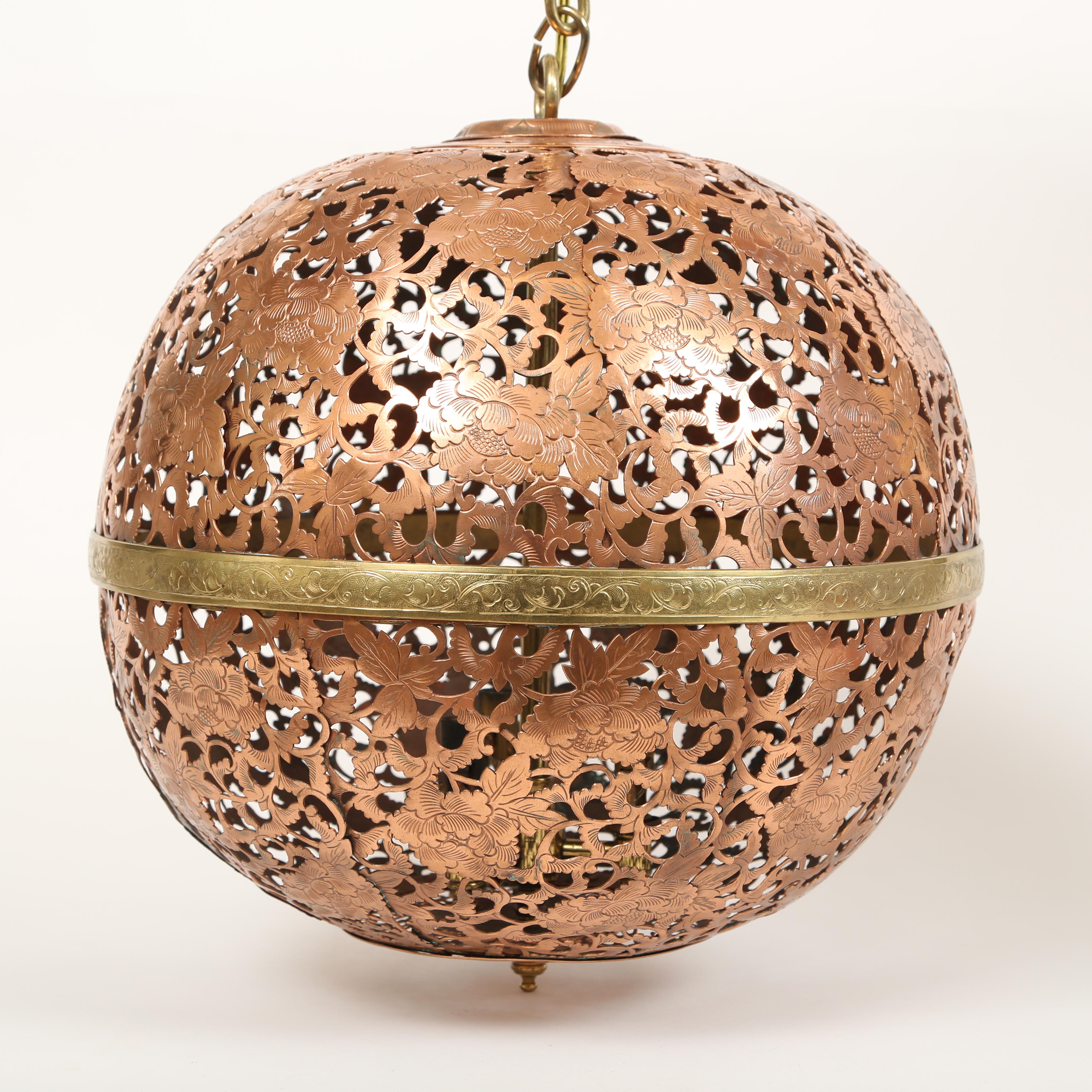 Round Moroccan lighting fixture on a chain with canopy. The copper fixture is pierced around a pattern of flowers, leaves and vines which are heavily engraved or chased. The canopy, chain and band around the middle of the fixture are all brass. The