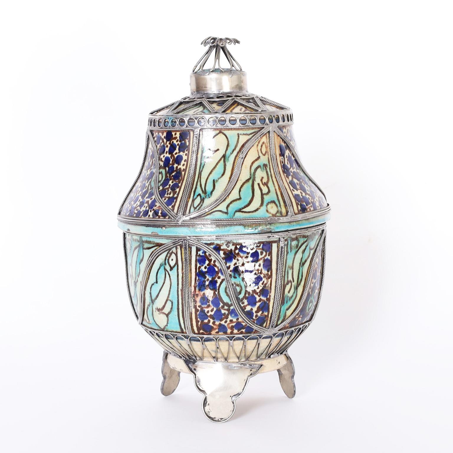 Striking glazed terra cotta urn decorated with floral designs in traditional mediterranean colors and having applied jewelry style metalwork that ups the wow factor.