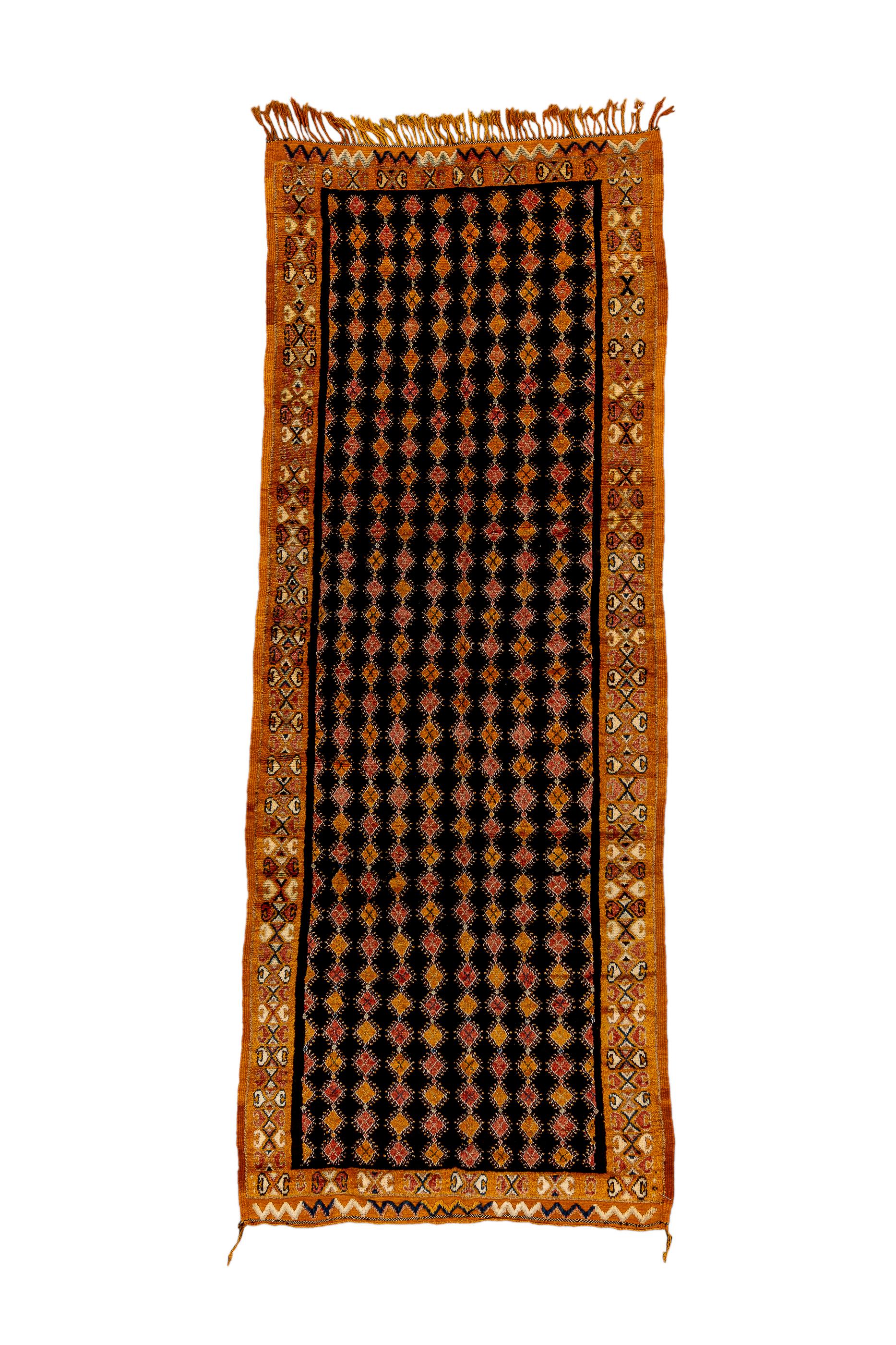 This lowlands piece shows a charcoal field with eight full and two half columns of little diamonds in red and tangerine. Tangerine border with C’s and X’s in a vaguely Turkish style. Narrow rust eteks (extra pile end panels) with polychrome zig-zag