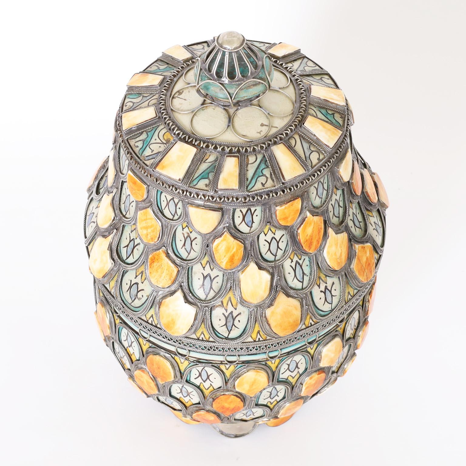 Lidded urn decorated with traditional mediterranean colors over terra cotta and bone, having applied jewelry style metal work that ups the wow factor.