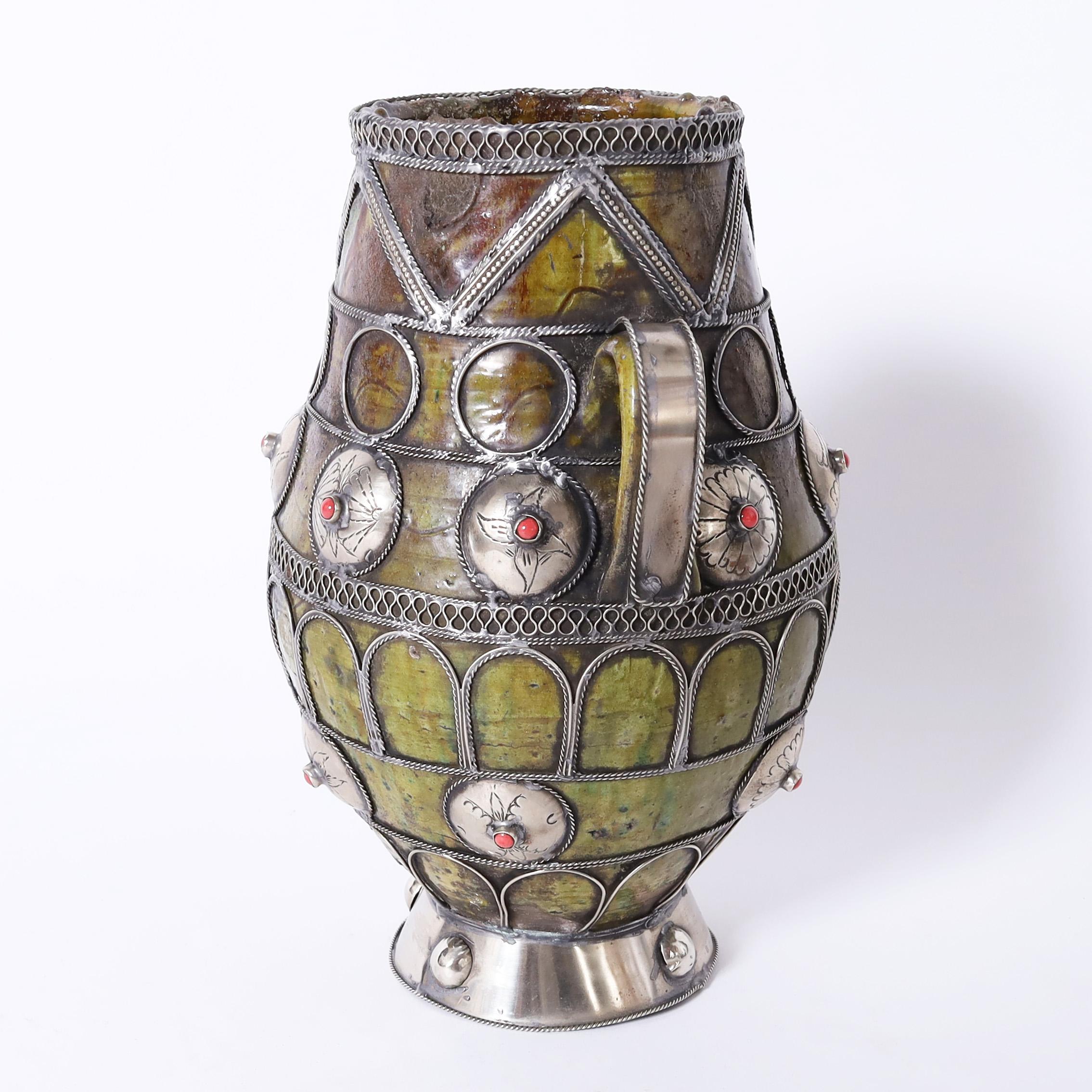 Standout vintage Moroccan vase handcrafted in terracotta in classic form with an olive tone glaze and decorated with jewelry like metalwork.