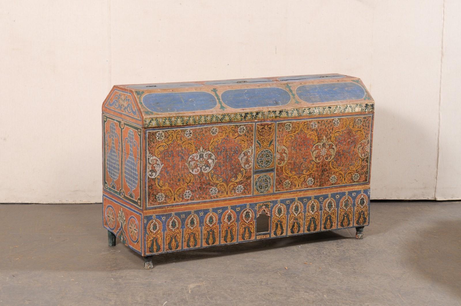 A Moroccan ornately painted-wood trunk from the early 20th century. This antique trunk from Morocco has has been artistically hand-painted in a geometric, foliate, and urn motif in vibrant shades of blue, orange, red, and gold. There is a skirt that