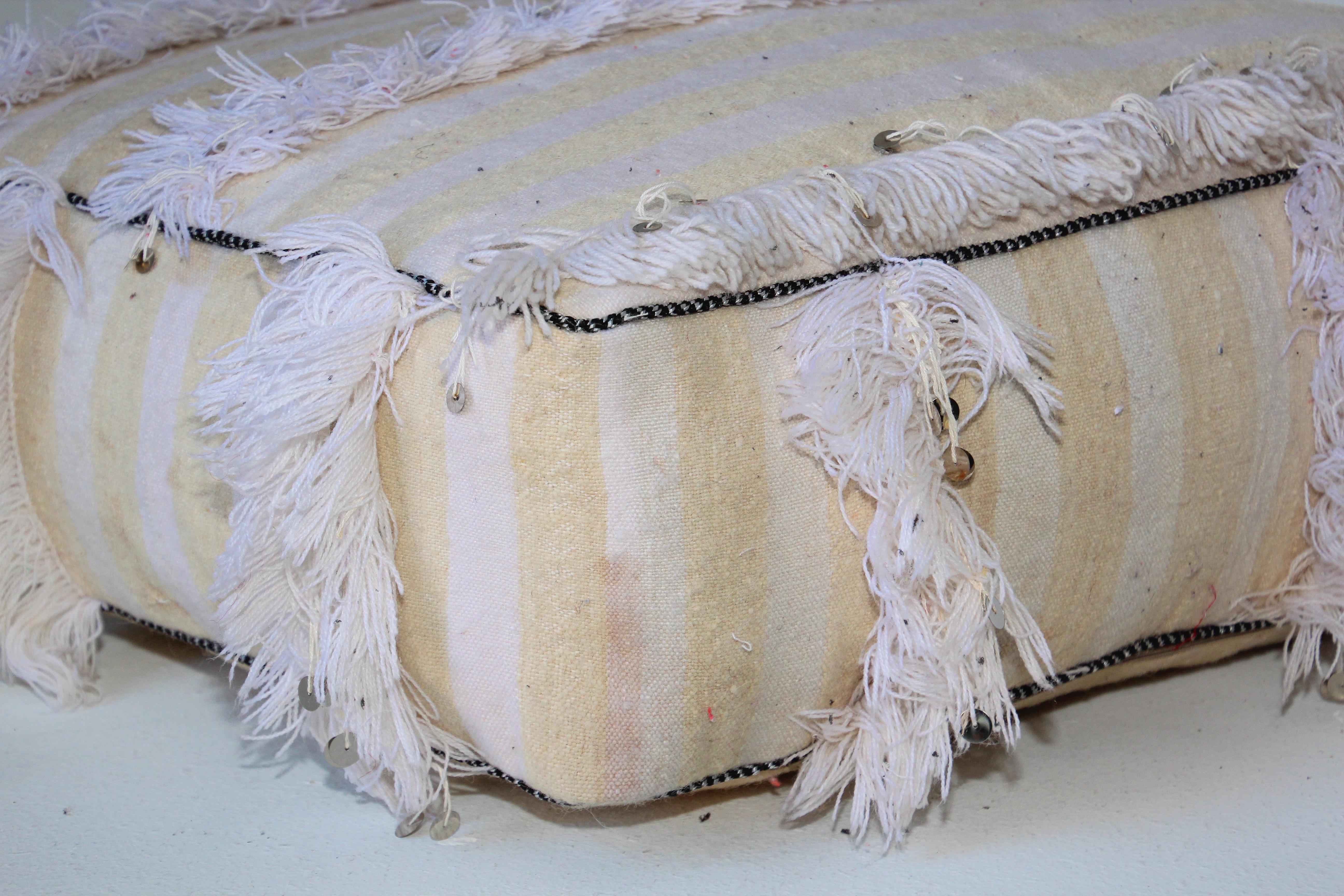 Moroccan floor pillow bohemian pouf with silver sequins and long fringes.
This handcrafted vintage Moroccan boho tribal floor pillow or pouf is made from a traditional handwoven white wool and cotton throw used by the Berber women in Morocco for