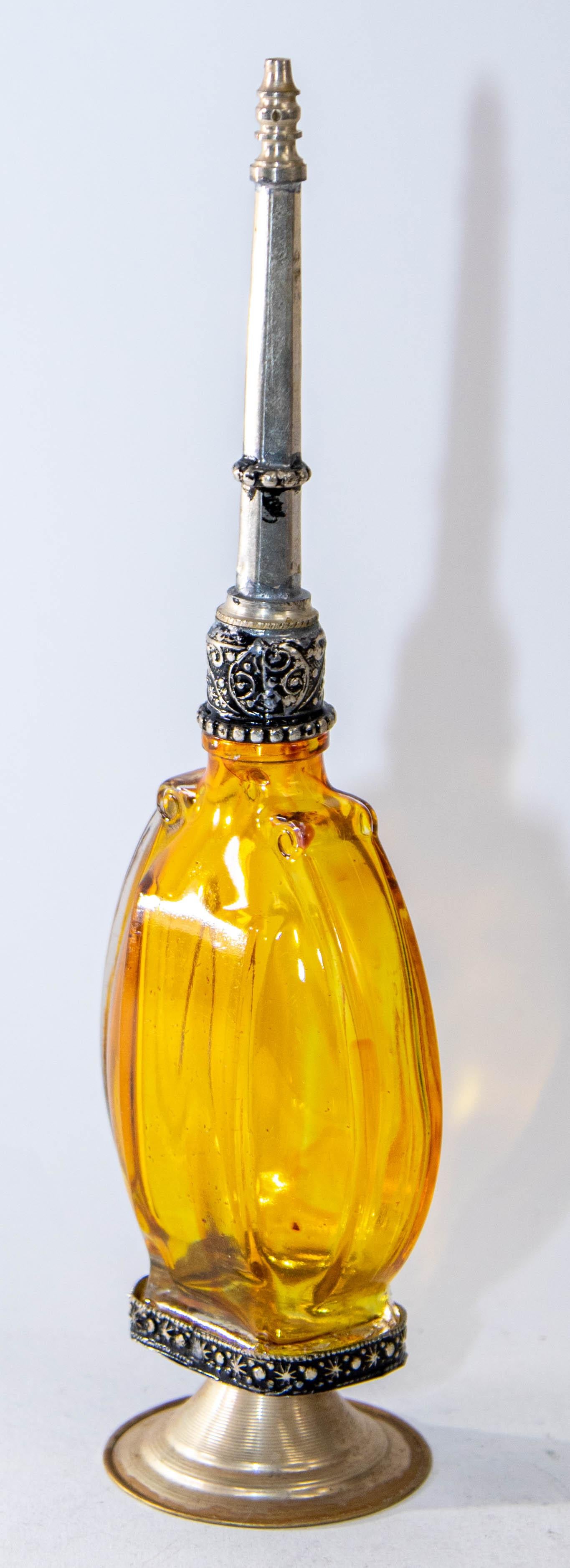 Handcrafted Moroccan Moorish footed glass perfume bottle or rose water sprinkler with raised embossed silvered metal floral design over amber yellow painted glass.
The pressed glass bottle in Art Deco, Art Nouveau style is oval shape with curved