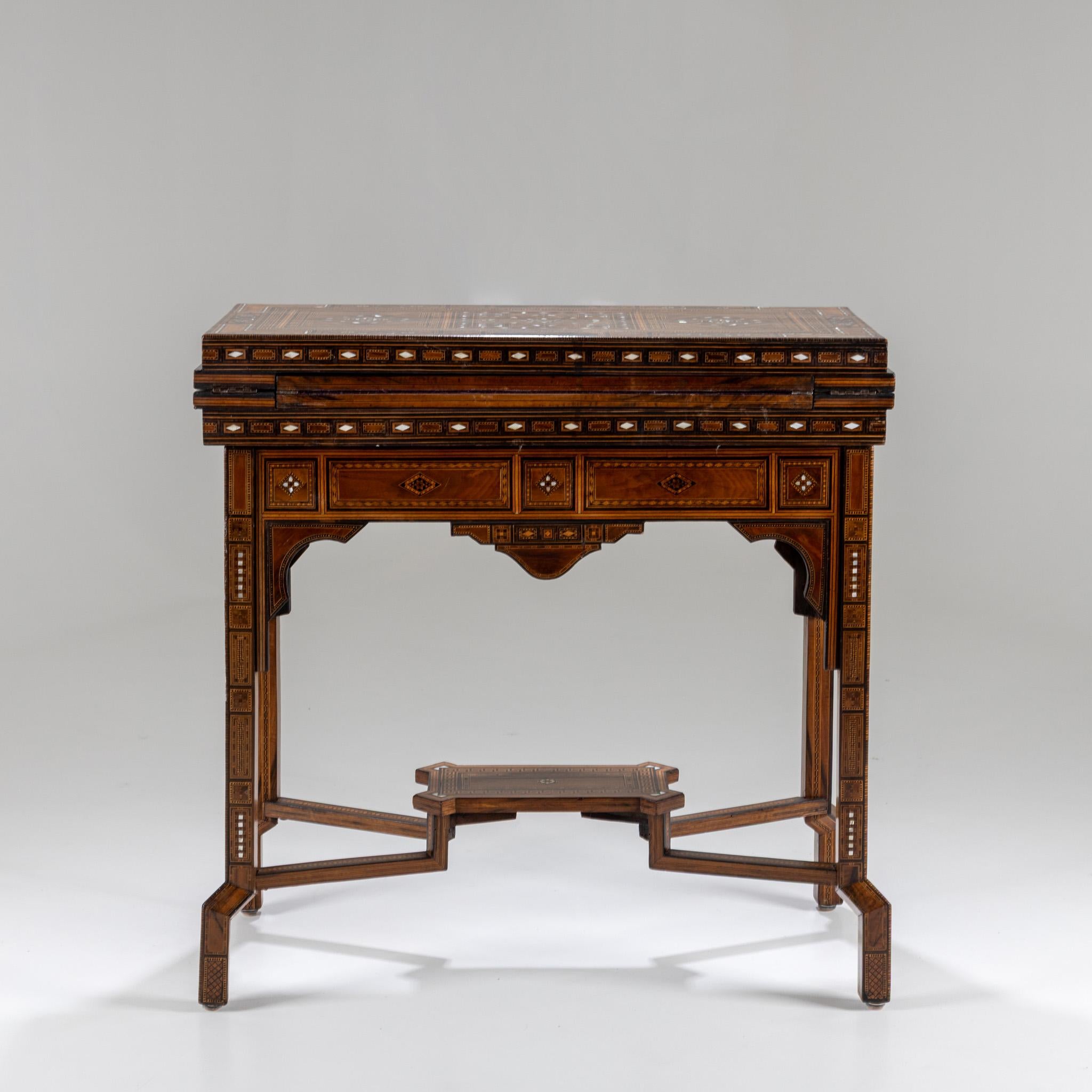 Game table in Moroccan style with intricately inlaid surfaces and a folding tabletop. The inside of the lid is lined with felt and serves as a playing surface. Beneath it are finely inlaid backgammon and chess boards. Dimensions when open: 82 × 90.5