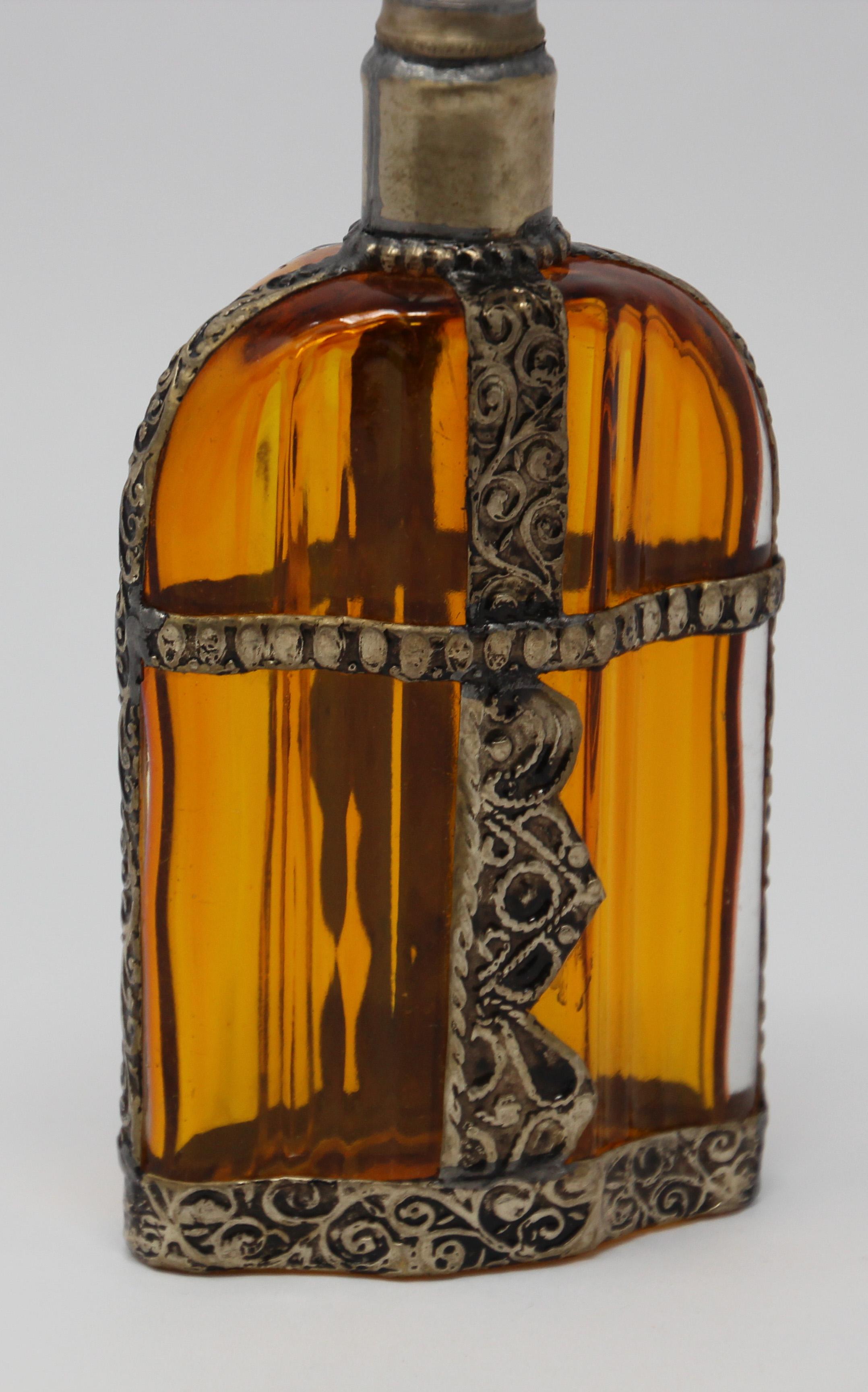 Handcrafted Moroccan Moorish amber painted glass perfume bottle or rose water sprinkler with raised embossed silvered metal floral design over amber glass.
The pressed glass bottle in Art Deco, Art Nouveau style is oval shape with curved sides and