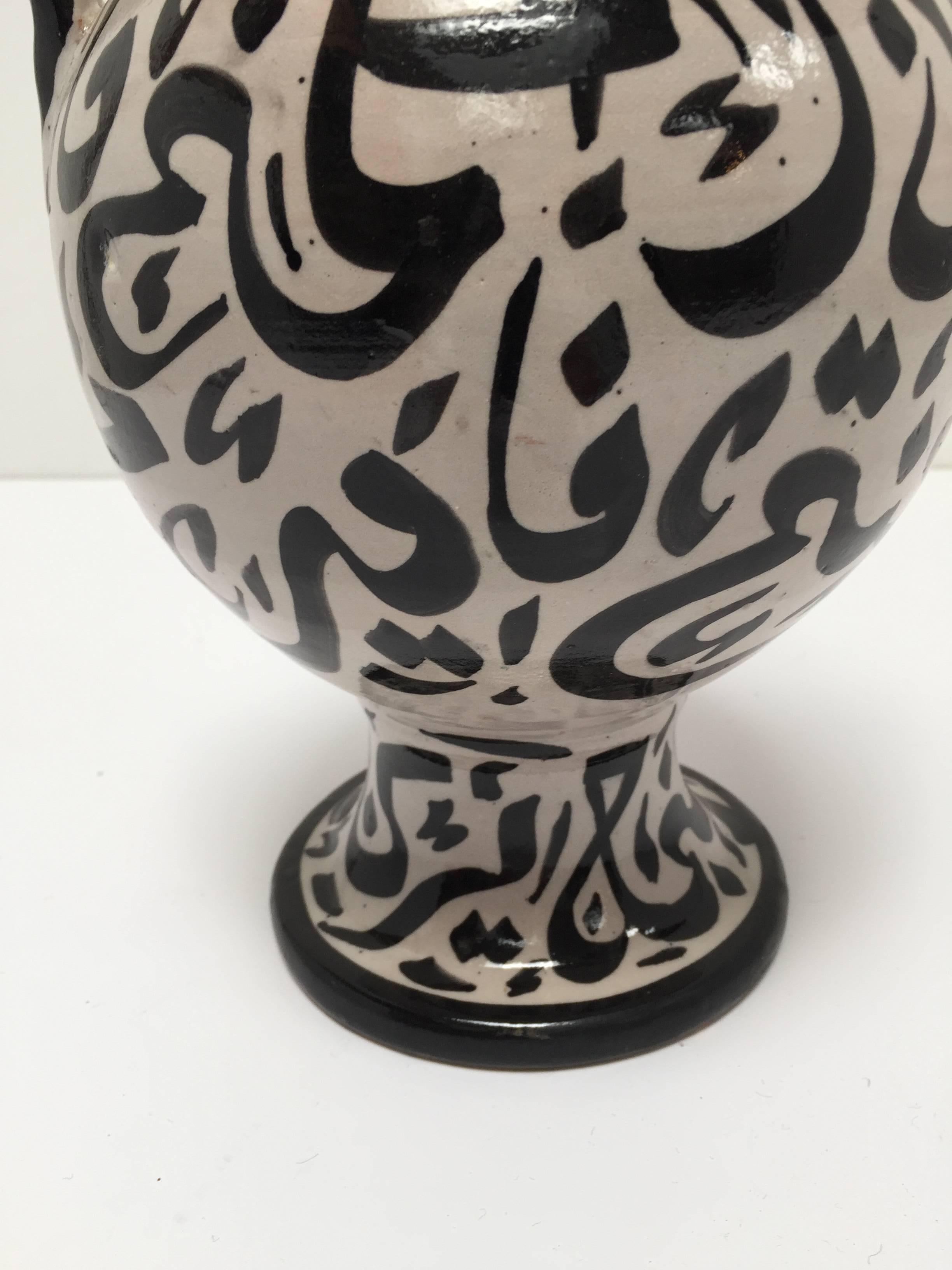 Moroccan glazed ceramic vase with handles from Fez. 
Moorish style ceramic handcrafted and hand painted in Fez with Arabic calligraphy writing design in black on ivory background.
This kind of Art Writing looks calligraphic is called Lettrism, it is
