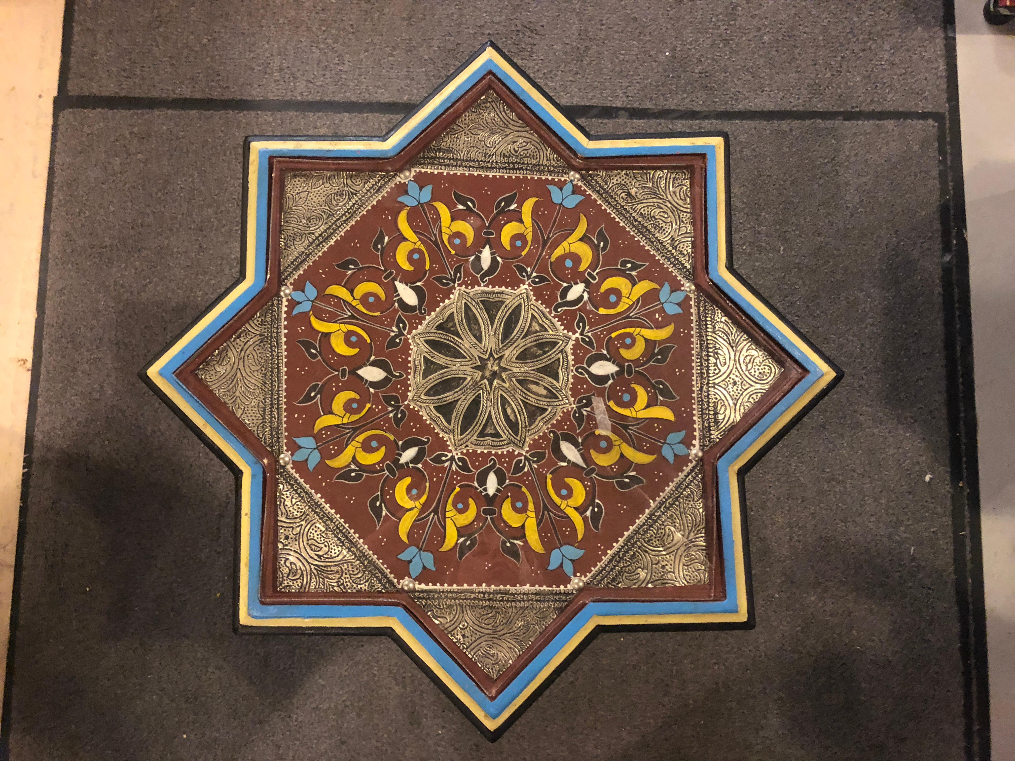 This astounding star-shaped wooden and brass inlaid table is an exotic and sophisticated addition to any room. Featuring a dazzling swirl of images, powerful color combinations and a beautifully realized Moorish component, you can be assured this