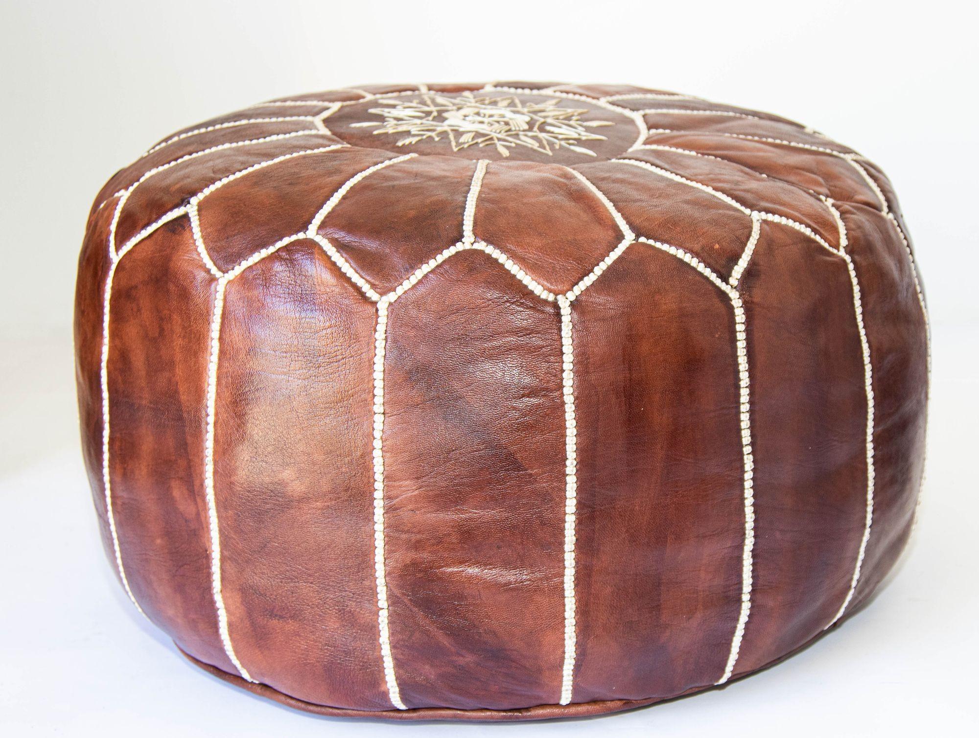 Puf marroquí de piel de camello marrón hecho a mano, con bordados.Podría usarse como taburete para los pies, o como mesa auxiliar u otomana.Los pufs marroquíes de piel están hechos a mano y bordados con banda de rodadura blanca.Muy bonito puf
