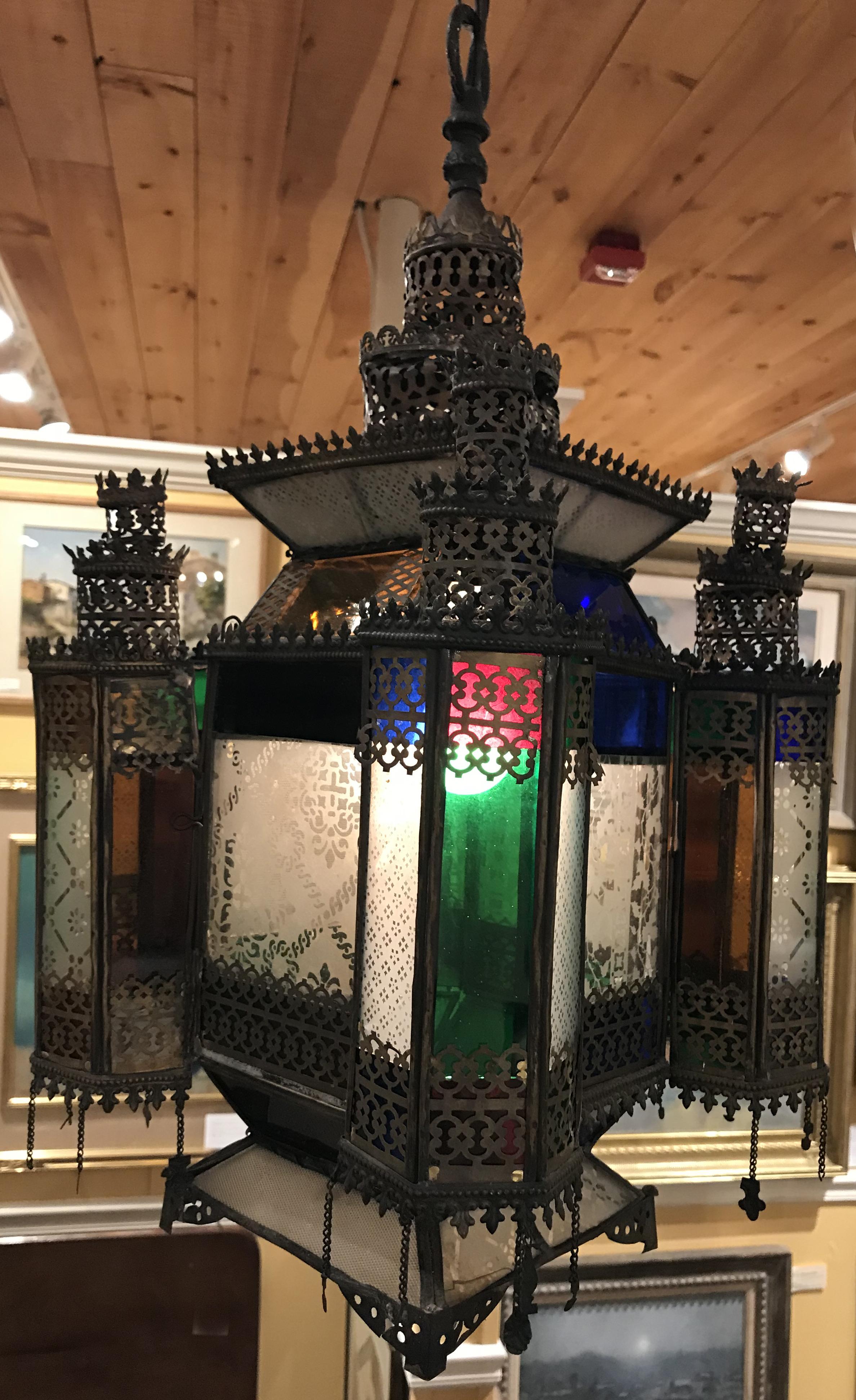 A fine example of a Moroccan hanging reticulated metal pendant lamp or lantern, with four large clear panels etched with foliate and geometric designs, accented with turret corners with various colored smaller panels, surrounding a single central