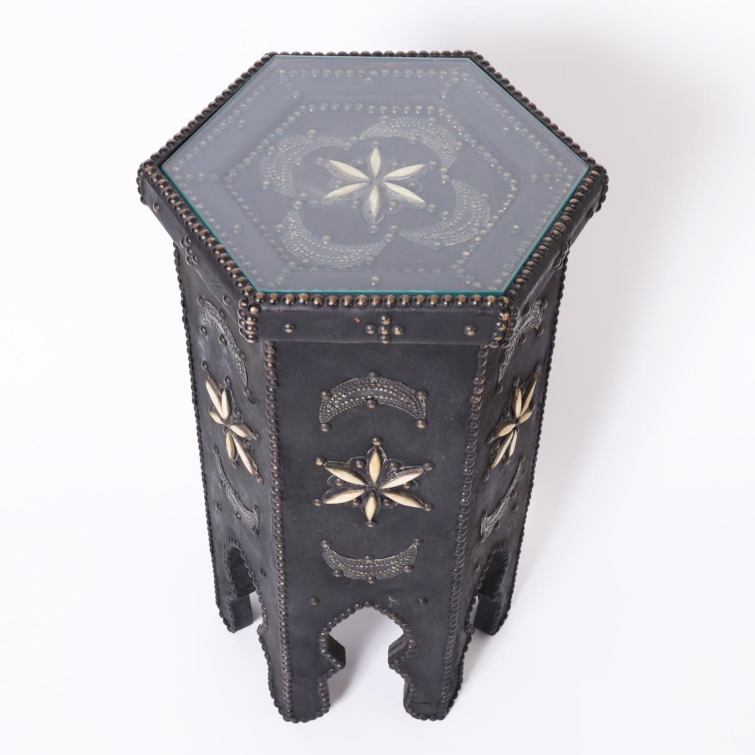 Rare antique Moroccan stand having a hexagon form entirely clad in leather decorated with brass tacks, crescent moons, and bone stars on six legs with moorish arches.