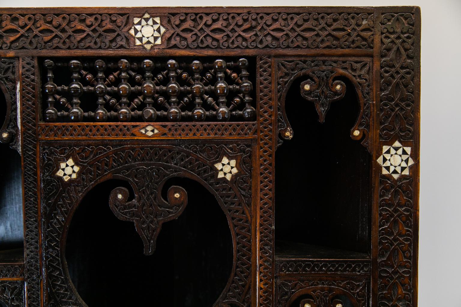 Moroccan inlaid corner cupboard, the front and shelves are profusely carved with geometric and stylized arabesque designs. It is inlaid with mother of pearl stars, diamonds, and circles. There are twelve arched openings which have pendant spearheads