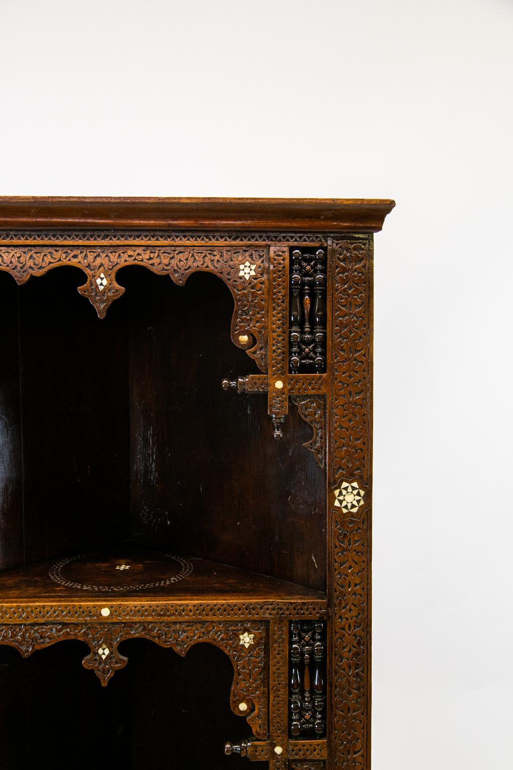 Moroccan inlaid corner cupboard, the front and shelves are profusely carved with geometric and stylized arabesque designs. It is inlaid with mother of pearl stars, diamonds, and circles. There are three arched openings. The shelves are inlaid with a