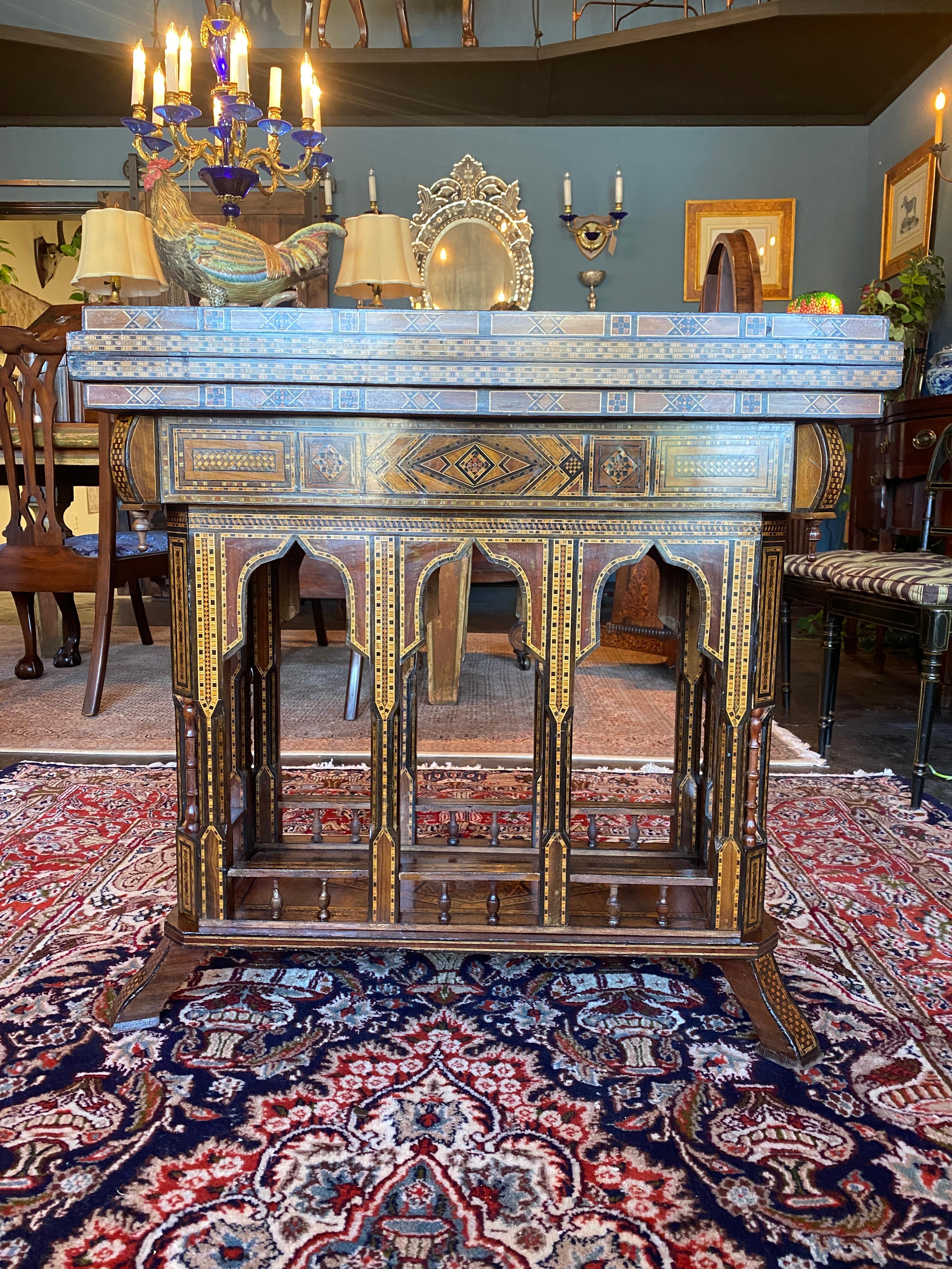 An intricately inlaid Moroccan gaming table. The swivel top opens to reveal three gaming surfaces. One velvet upholstered card table top with an inlaid checkers board on the opposite surface. This surface is removable to reveal a Backgammon board.