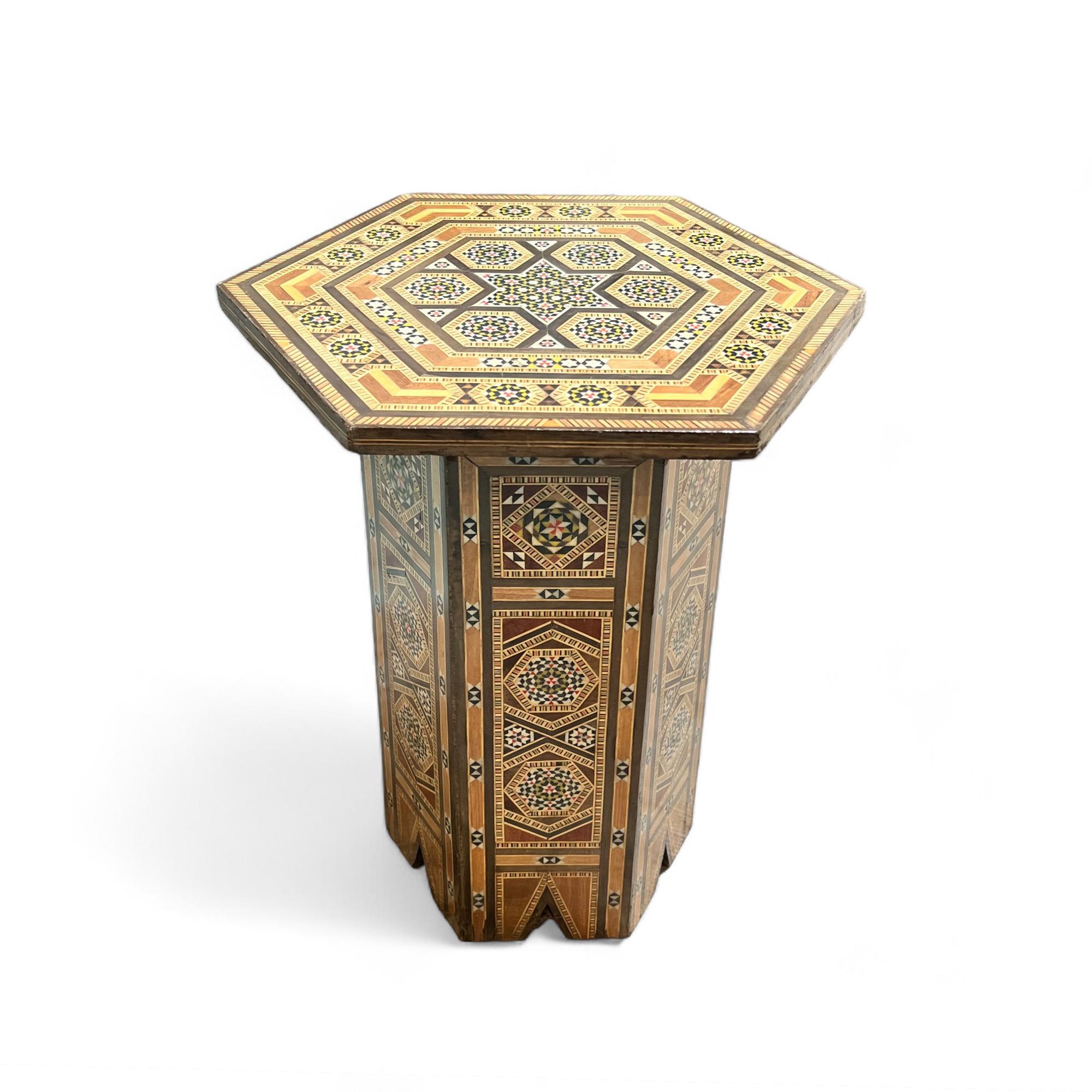 This elegant Moroccan inlay side table features a hexagonal design, intricately decorated with geometric patterns and inlaid with various colorful woods. The detailed craftsmanship and symmetrical design make it a stunning piece that adds a touch of