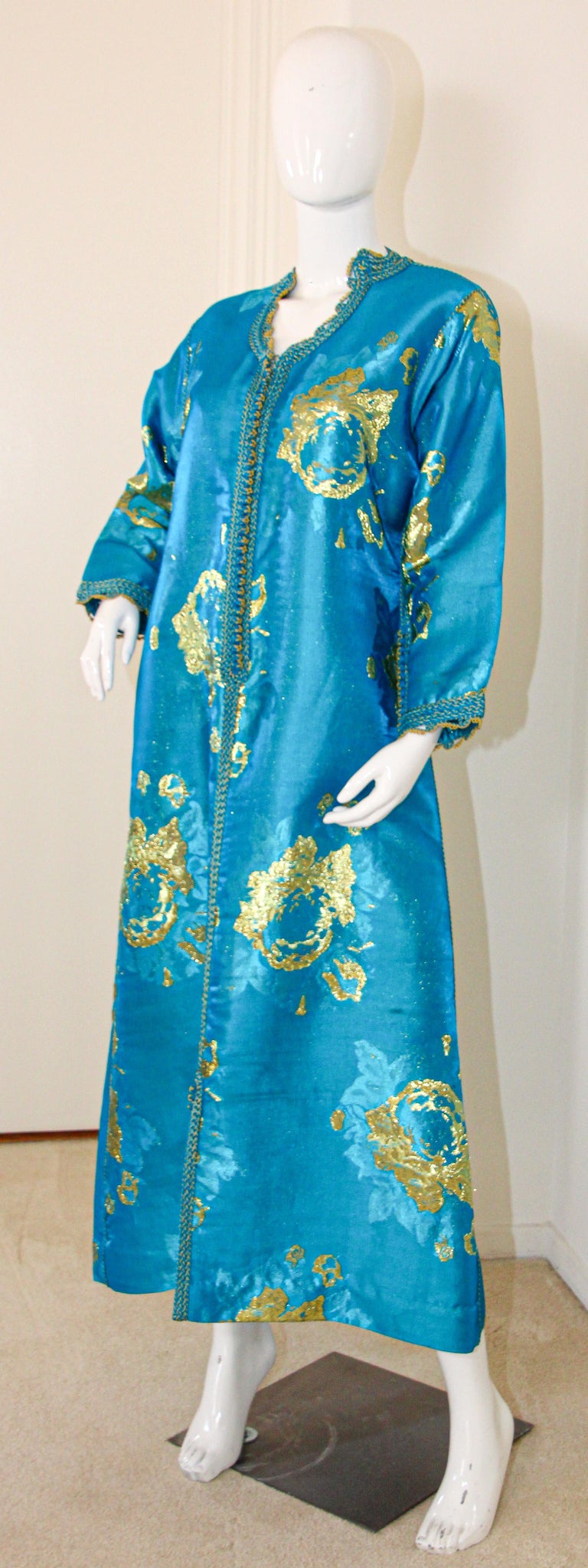Elegant Moroccan caftan in turquoise and gold floral lame metallic and embroidered trim,
circa 1970s.
This long maxi dress kaftan is embroidered and embellished entirely by hand detailing around neckline, shoulders and cuffs.
It’s crafted in Morocco