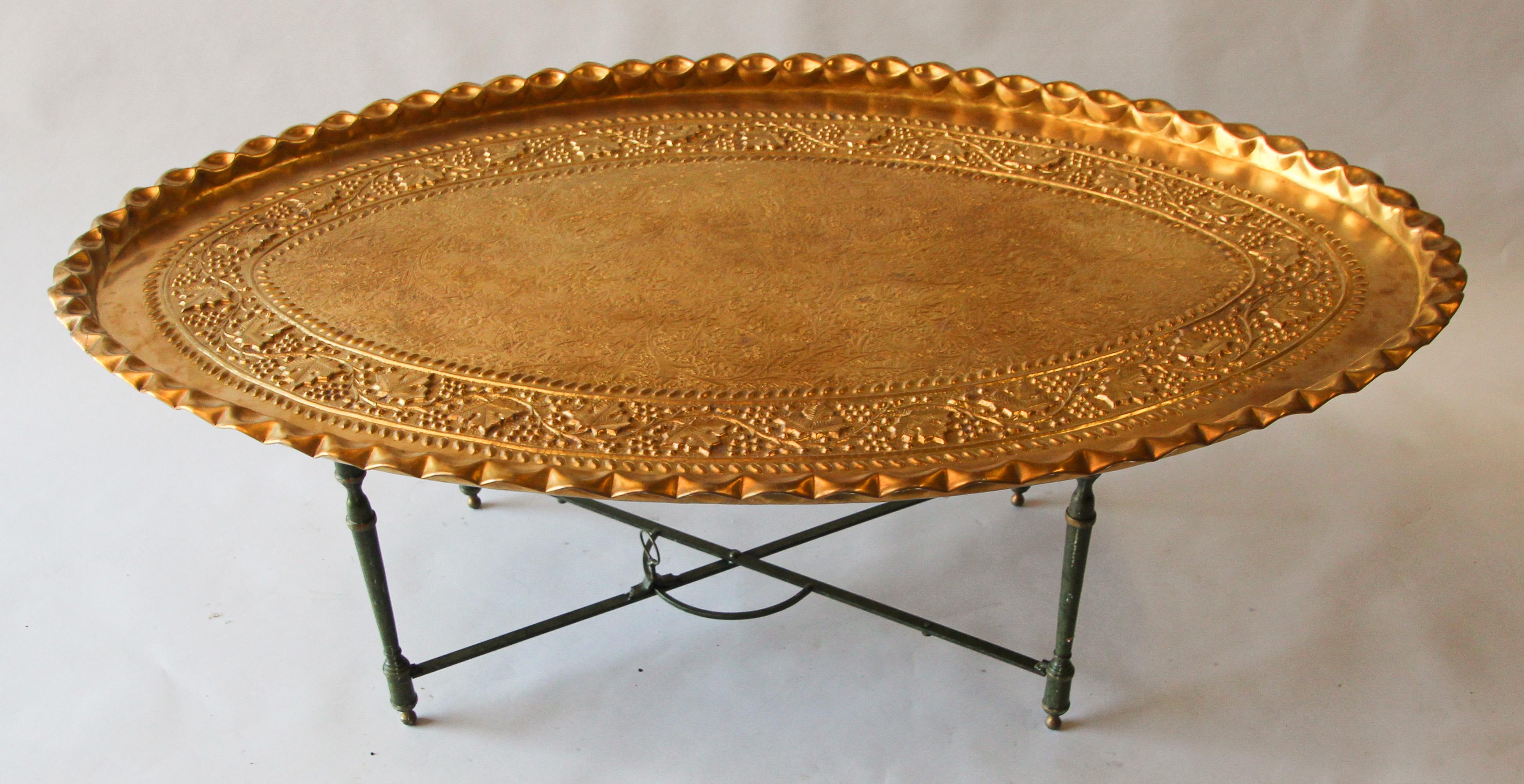 Very large Moroccan oval polished brass tray table.
Beautifully hand chiseled and hand-hammered with exquisite floral and geometric designs and pie crust edging and some cut-out designs. 
The tray sits on a metal folding base.
Dimensions: 53.5