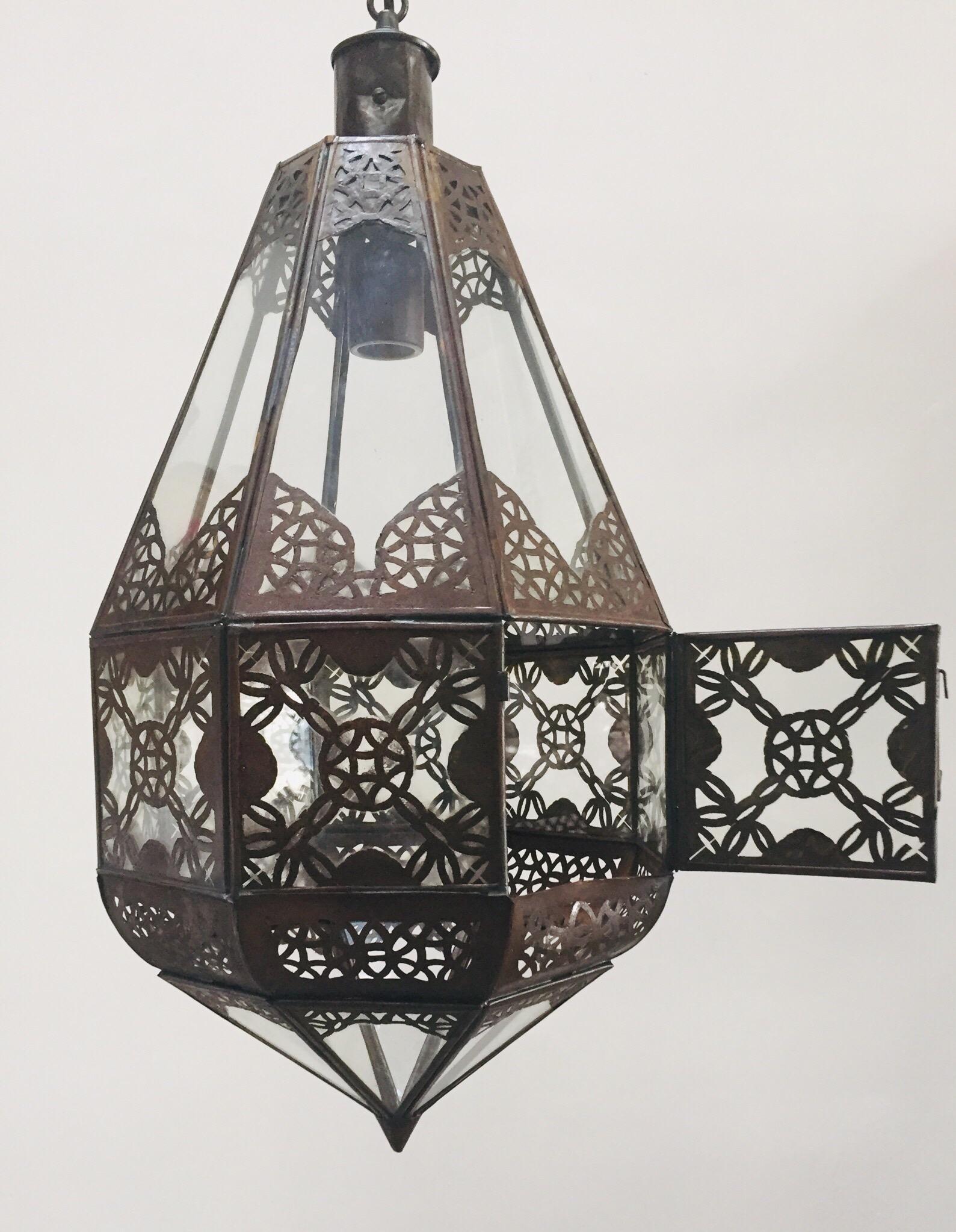 Lanterne marocaine en verre transparent, fabriquée à la main.
Métal finition bronze antique rouillé avec motif ajouré en filigrane mauresque.
Ce luminaire marocain est recâblé pour recevoir une ampoule, des chaînes de 3 pieds et un
