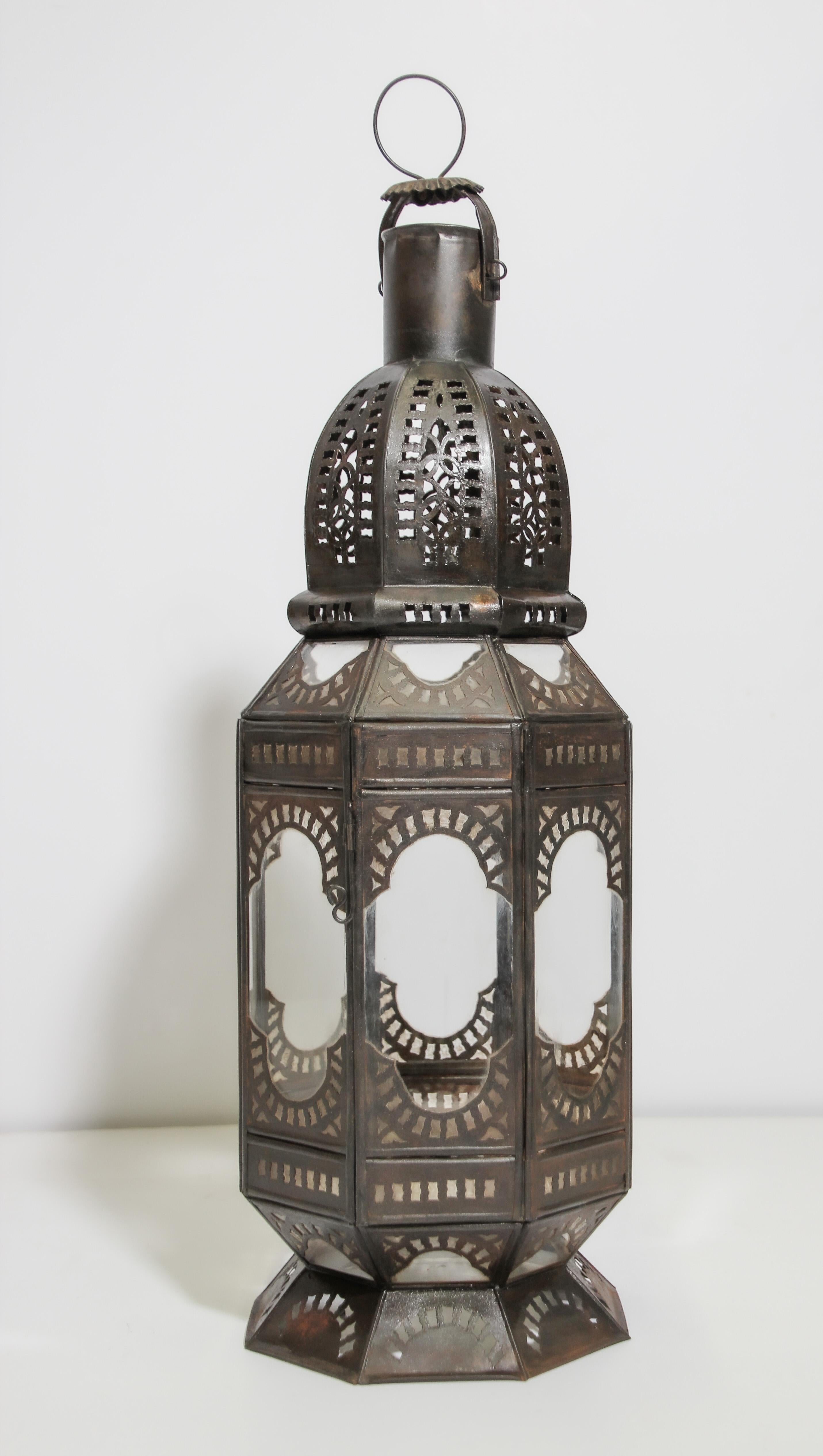 Handcrafted Moroccan clear glass lantern in octagonal shape adorned with hand-cut metal Moorish filigree designs. Hurricane candle lamp open metal work design with clear glass. There is a small door to access the inside. The lantern has a small door