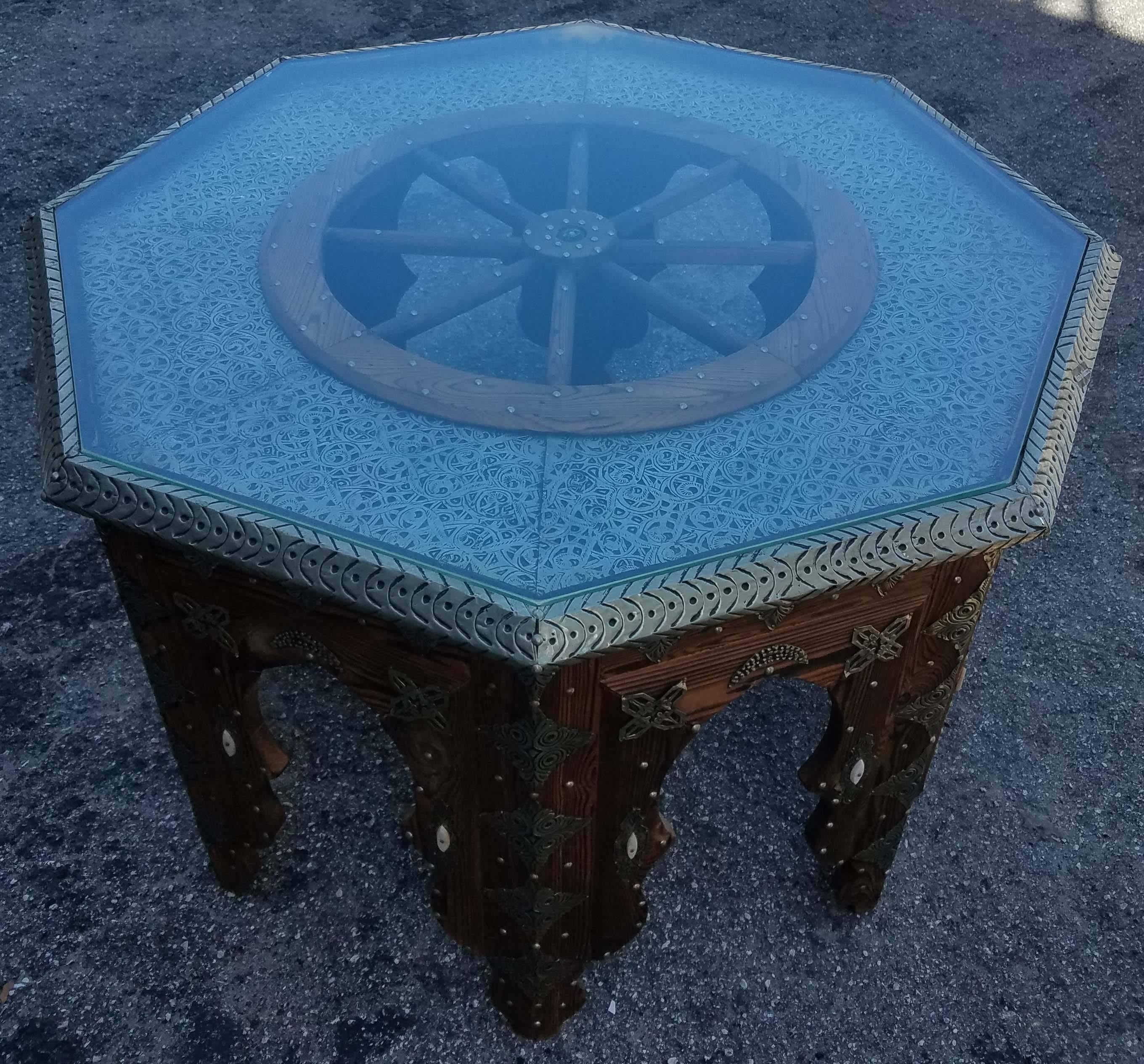 Very exotic hand-carved and metal inlaid Moroccan coffee table. Adorned with detailed carving along the sides and the top, and its ship’s wheel in the center, this table will sure be a excellent add-on to your décor. It measures approximately 37